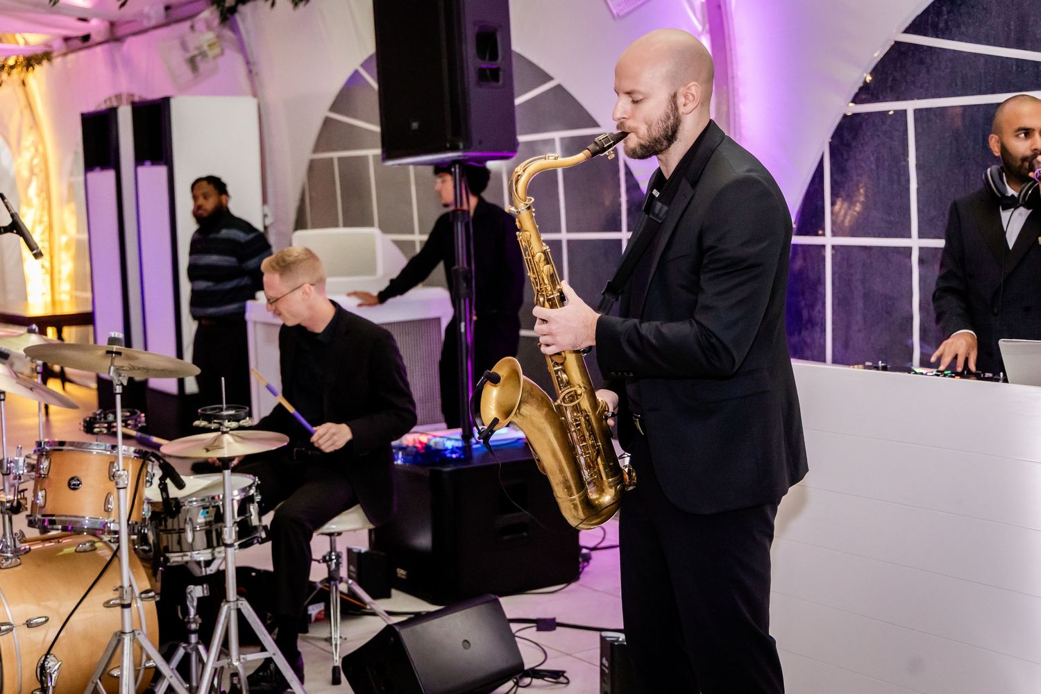 Live band performing at an elegant wedding reception with instruments and purple lighting.