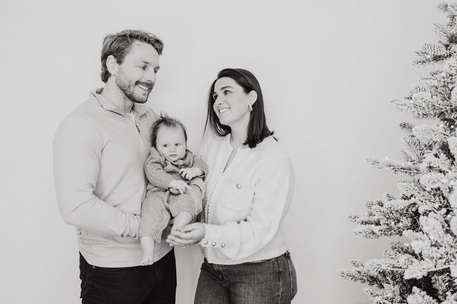 Black and white photo of a couple holding a baby in front of a Christmas tree.