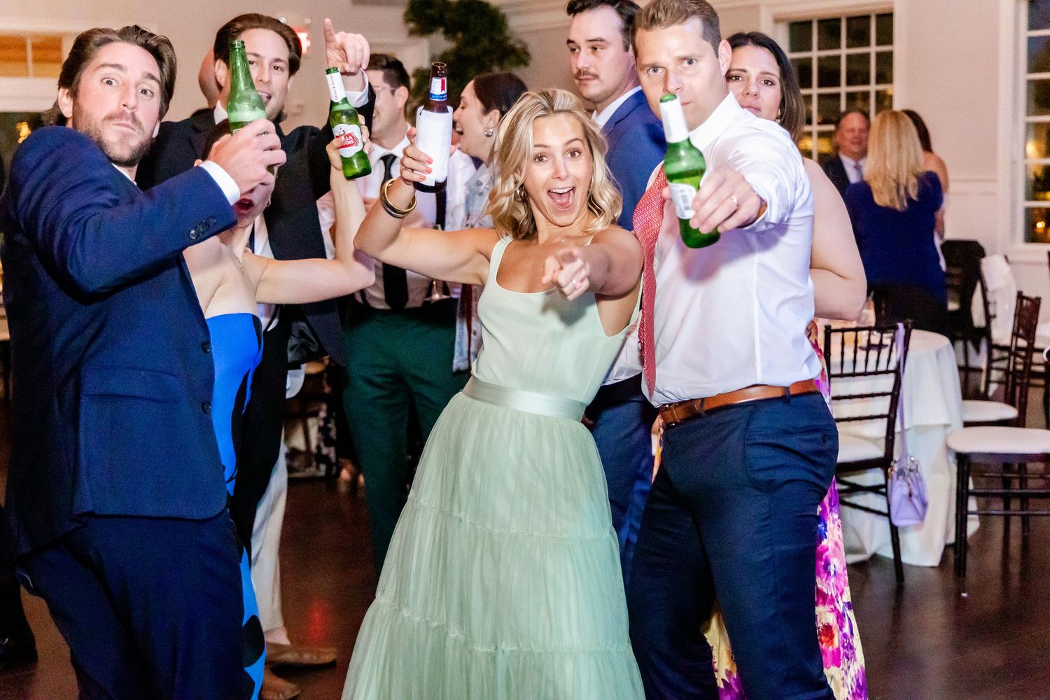 Party guests pose together holding beer bottles at a wedding reception.