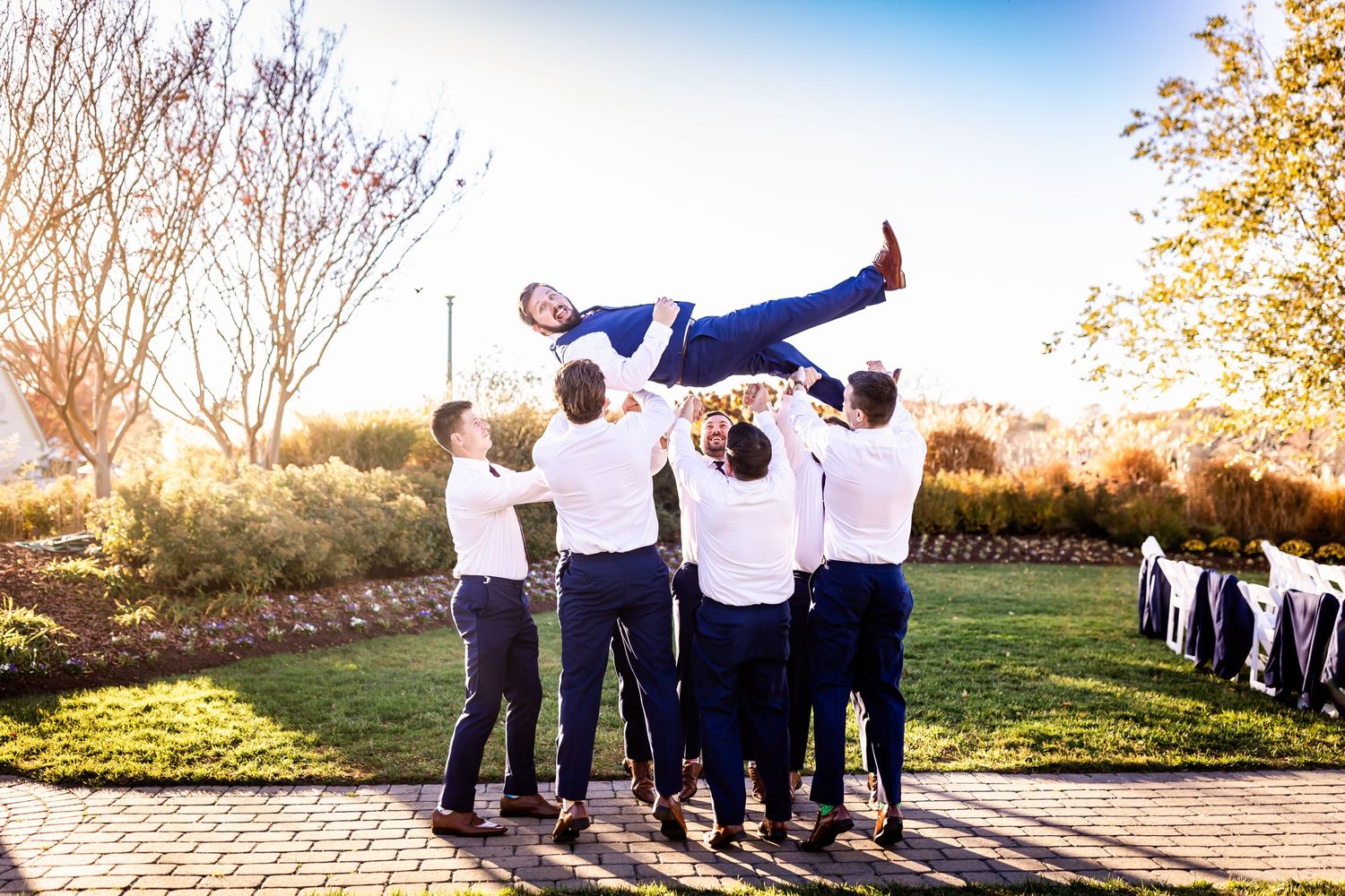 Groomsmen playfully toss someone in the air during outdoor wedding photo session.