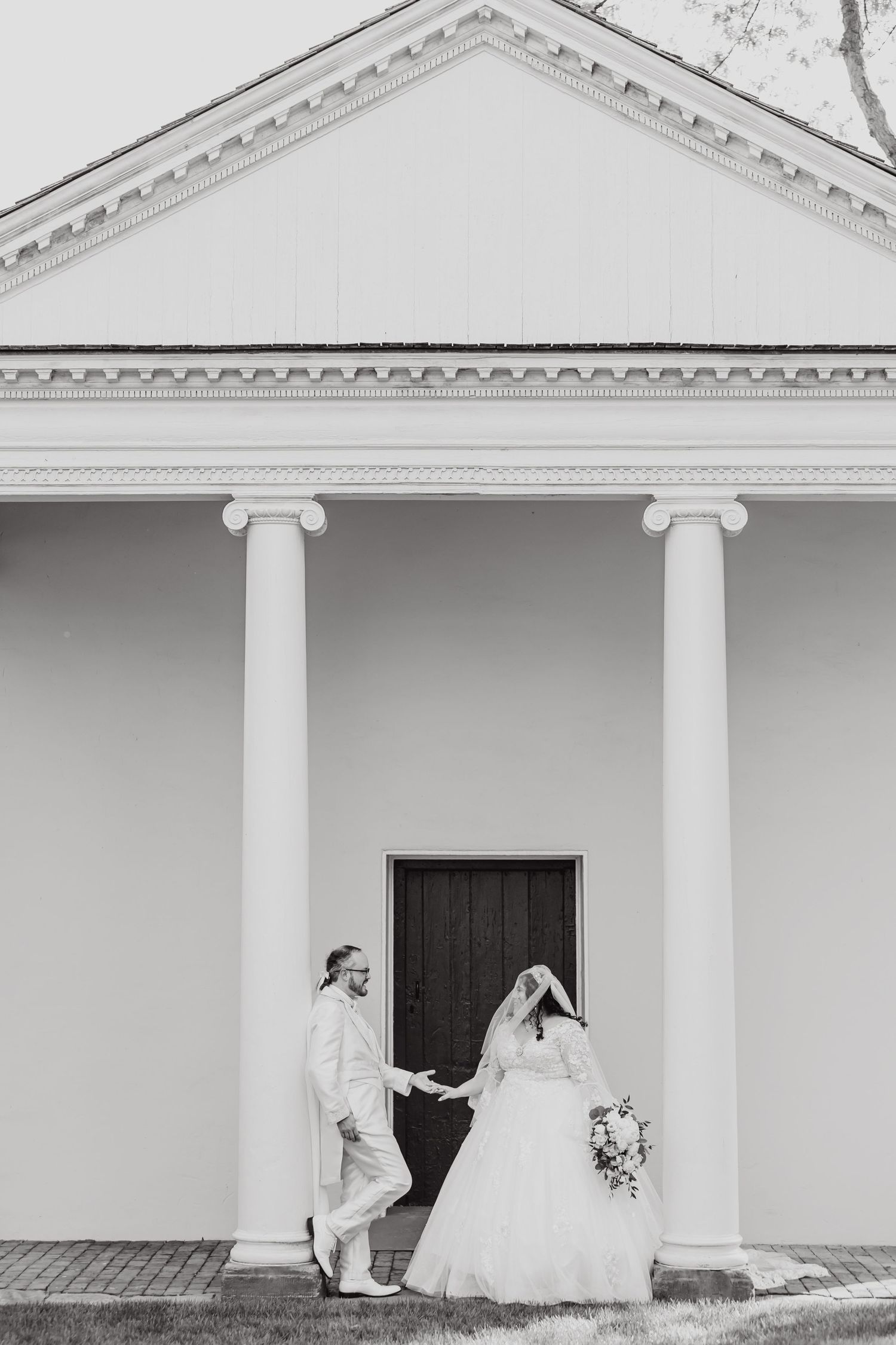 Black and white wedding photo showing couple posing by classical building entrance.