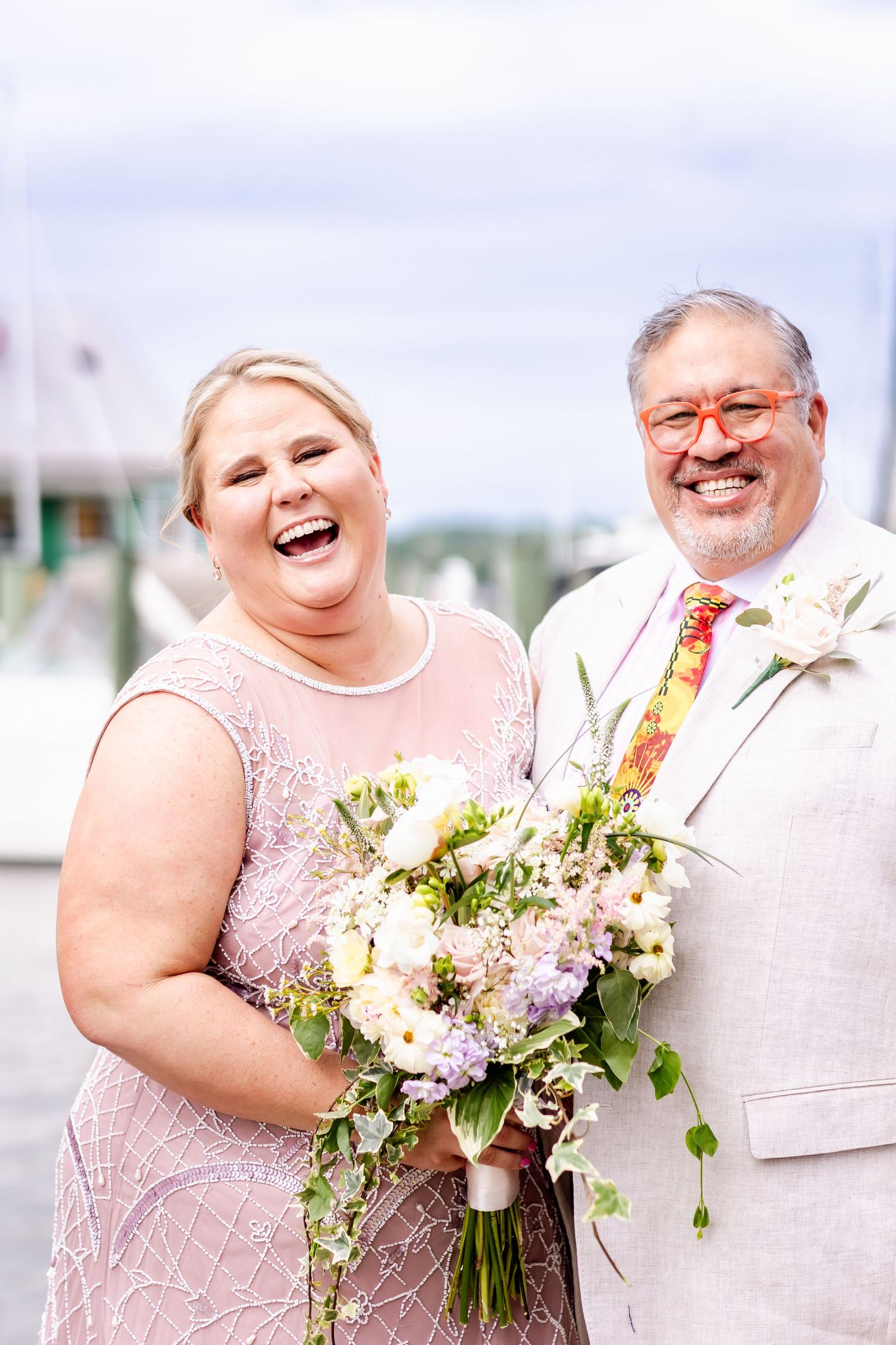 A joyful moment captured at a marina with a couple in matching pink and white formal attire.