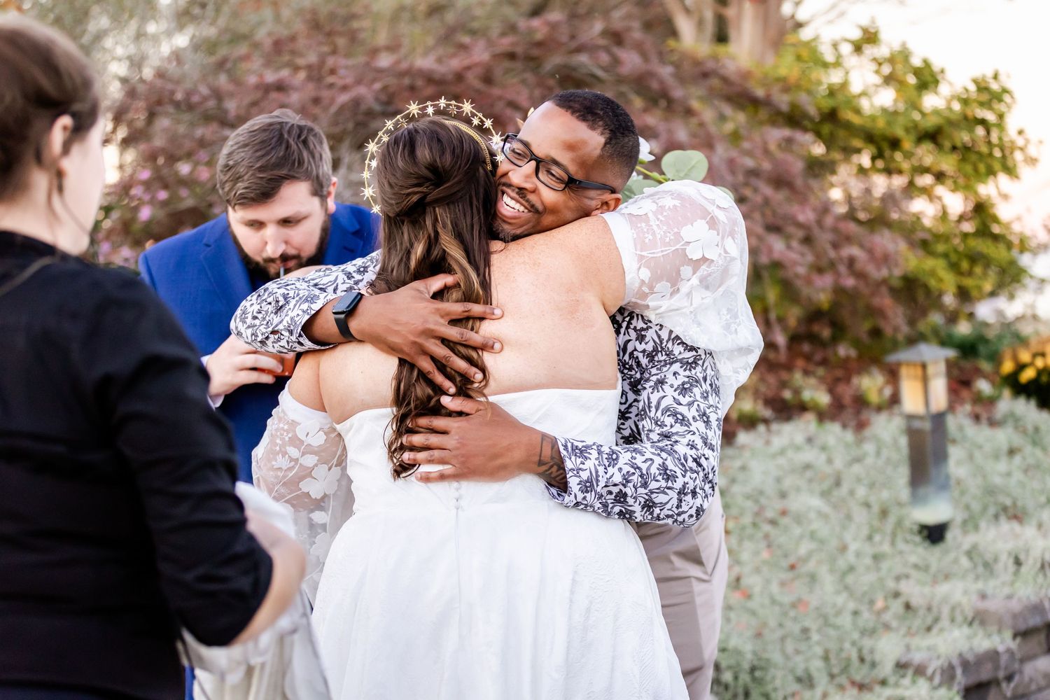 Wedding guests embrace during emotional reception moment outdoors.