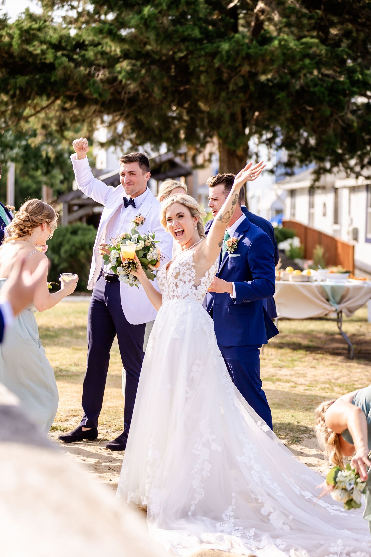 Wedding party celebrates joyfully outdoors with parties in white dress and navy suit holding yellow flower bouquets.