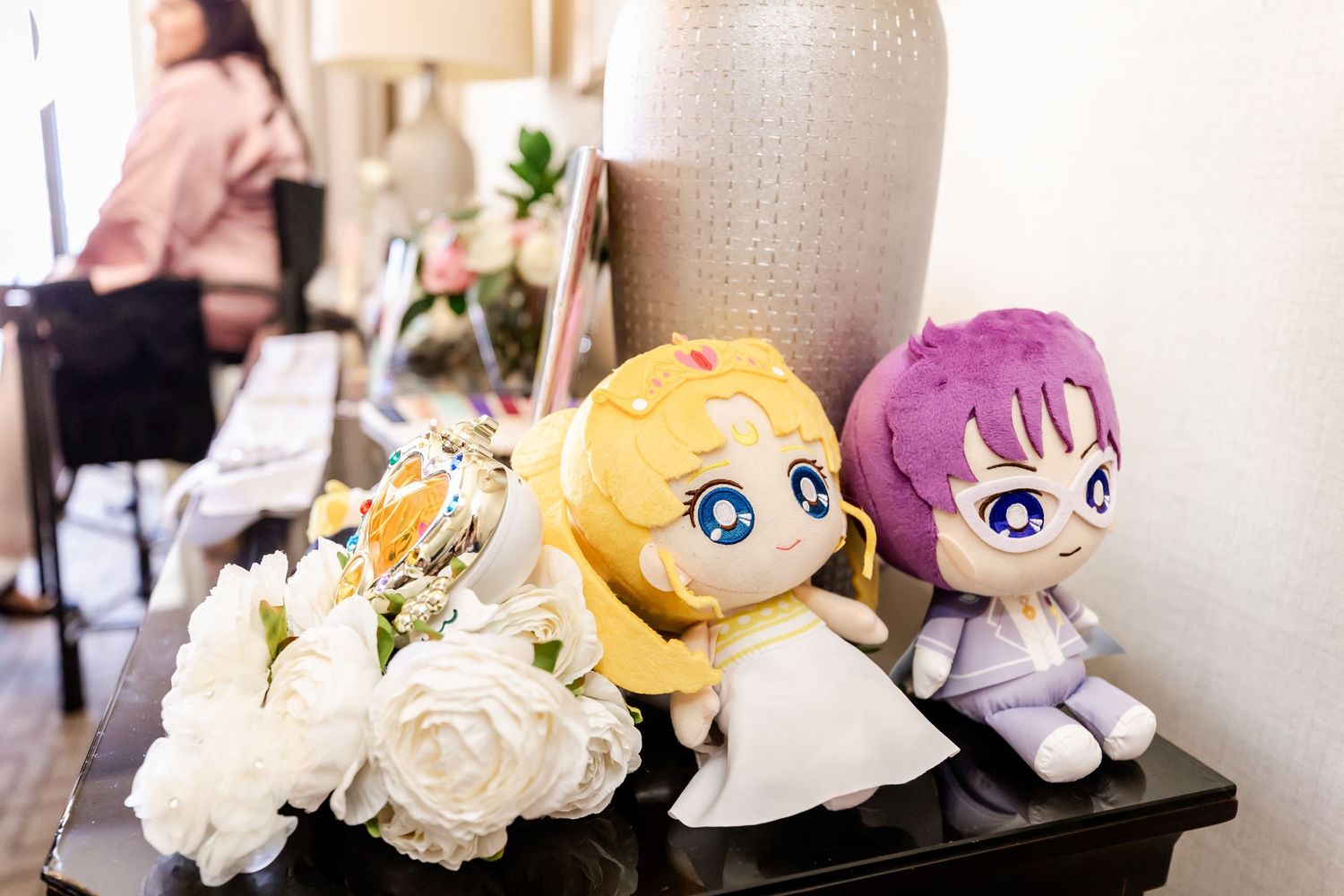 Anime character plush dolls and white roses arranged near a decorative vase.