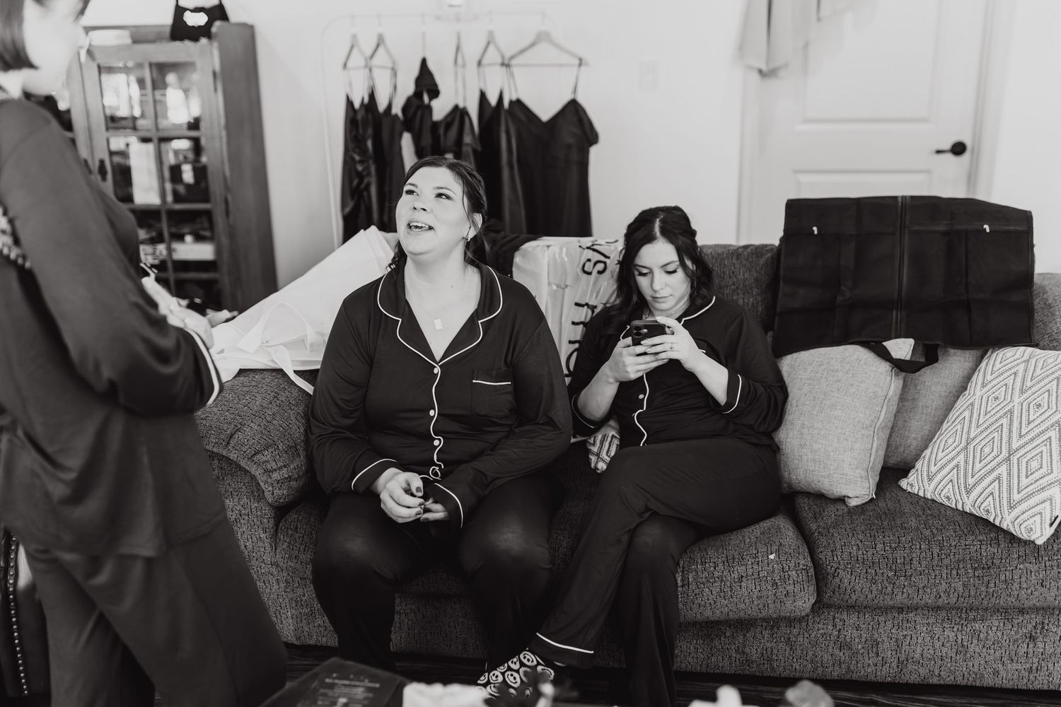 Two friends share a relaxed moment laughing together on a couch during wedding preparations.