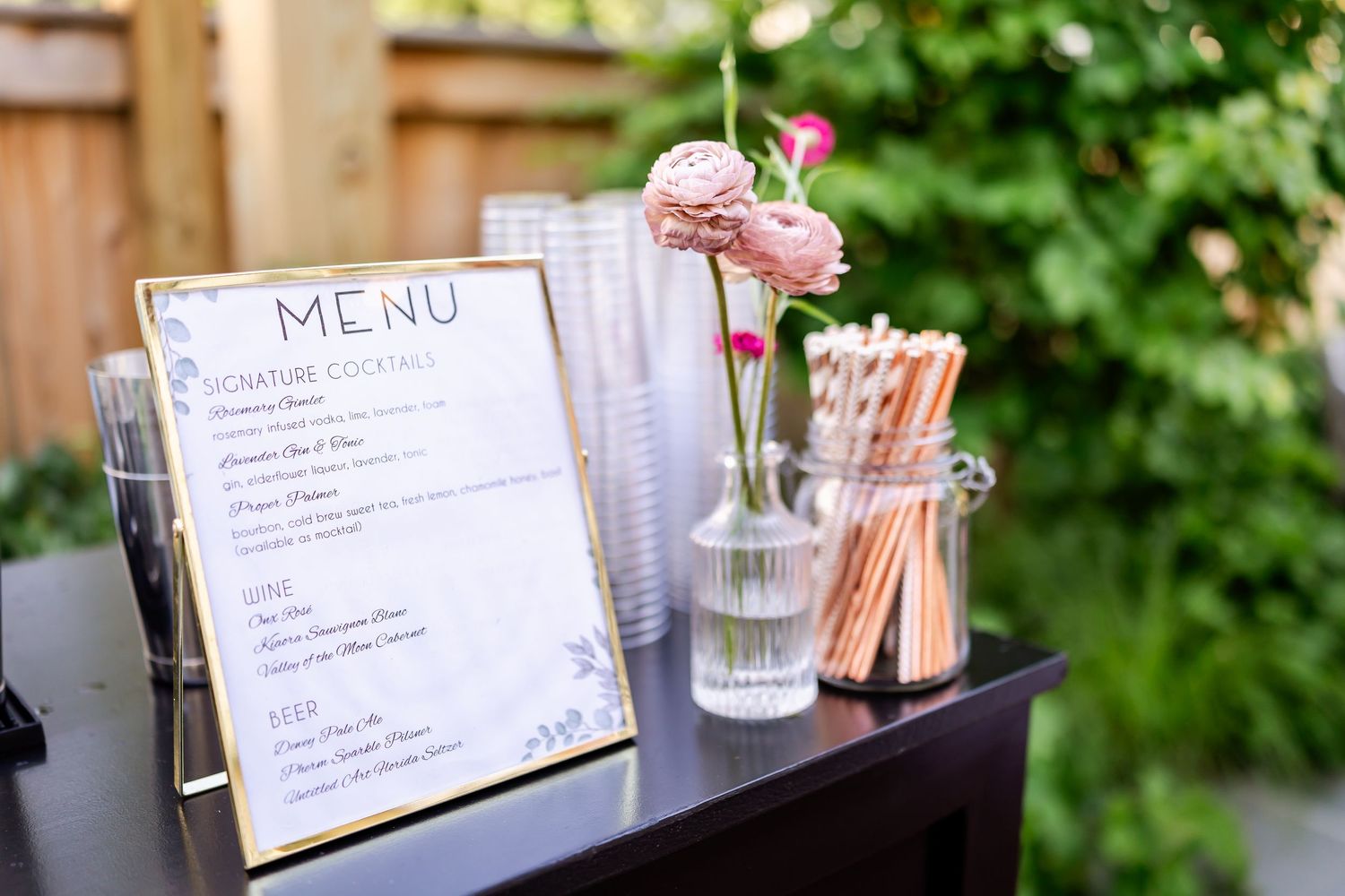 Wedding menu display with handwritten text and pink flower in vase.