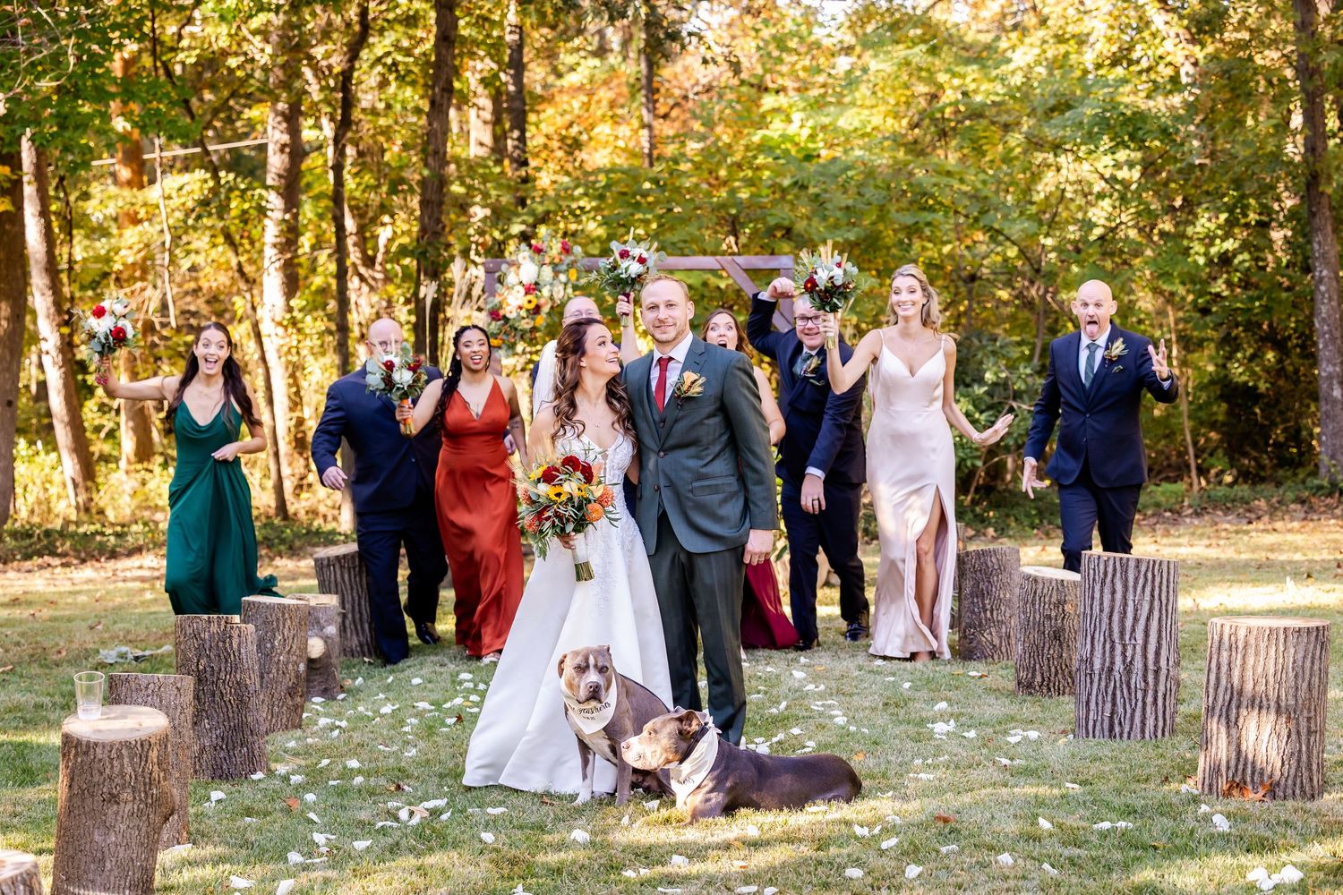 Wedding party poses outdoors in a scenic wooded area with autumn foliage and natural lighting.