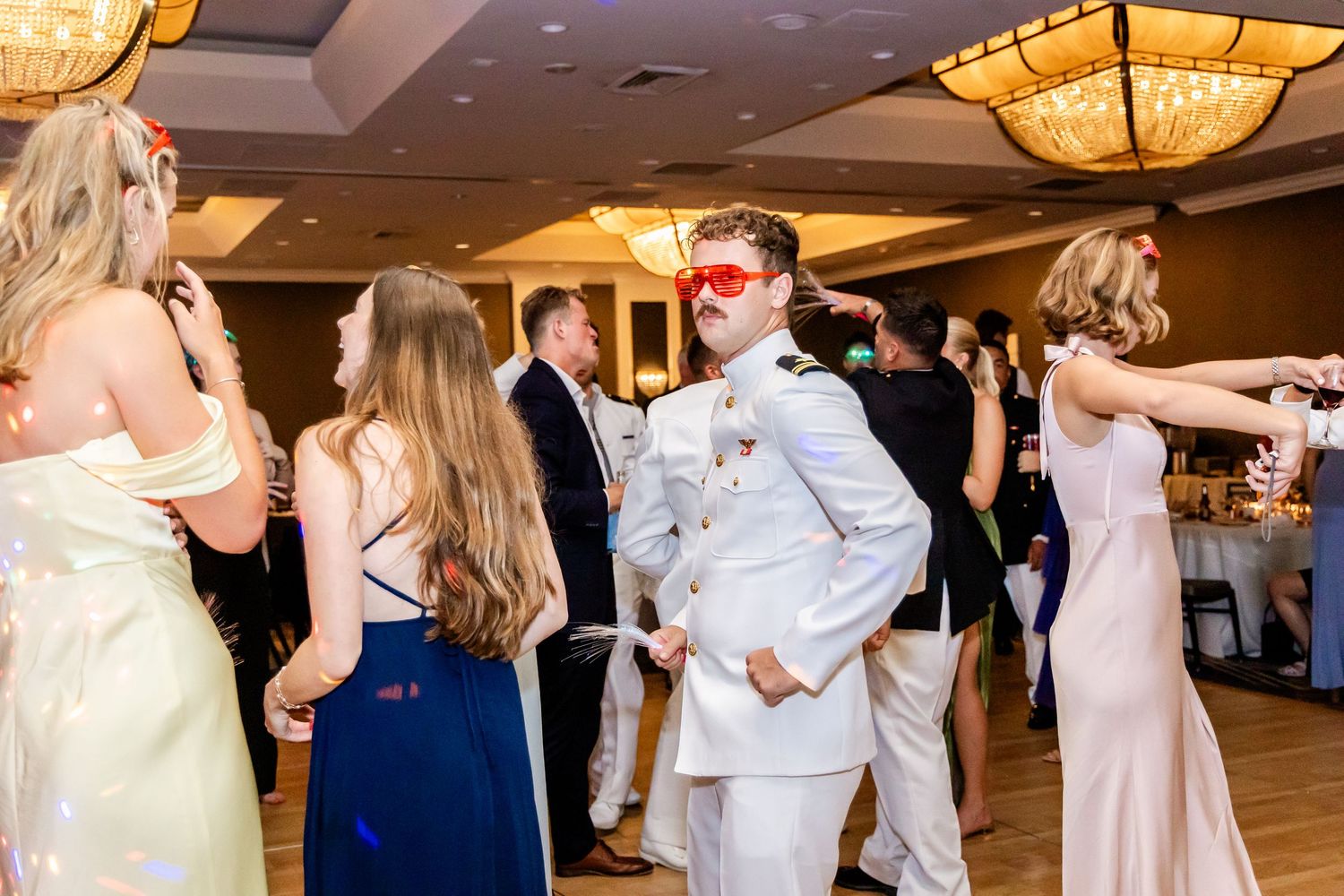 Wedding guests dancing and celebrating with props on the ballroom dance floor.