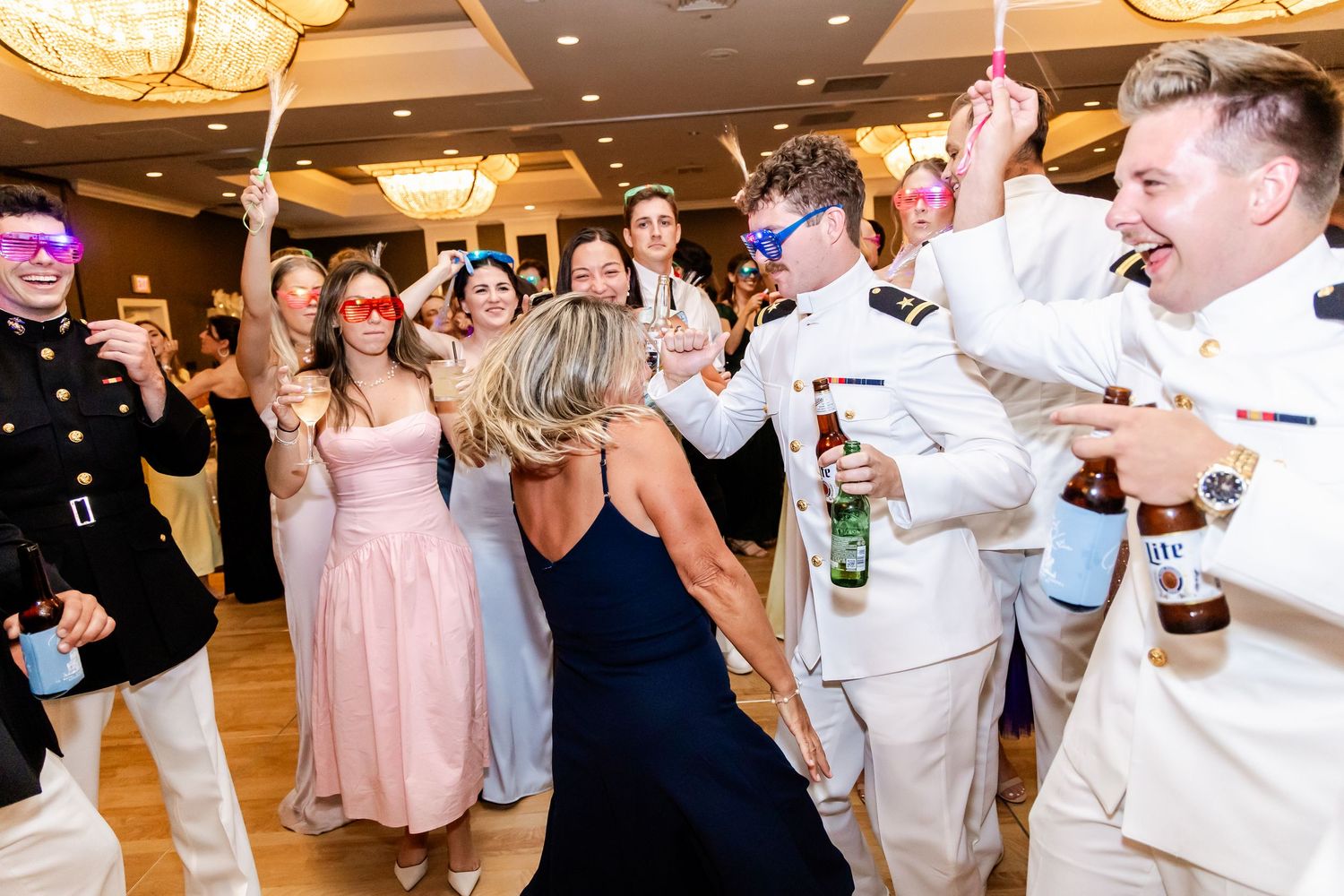 Lively wedding reception celebration with guests dancing and raising drinks.