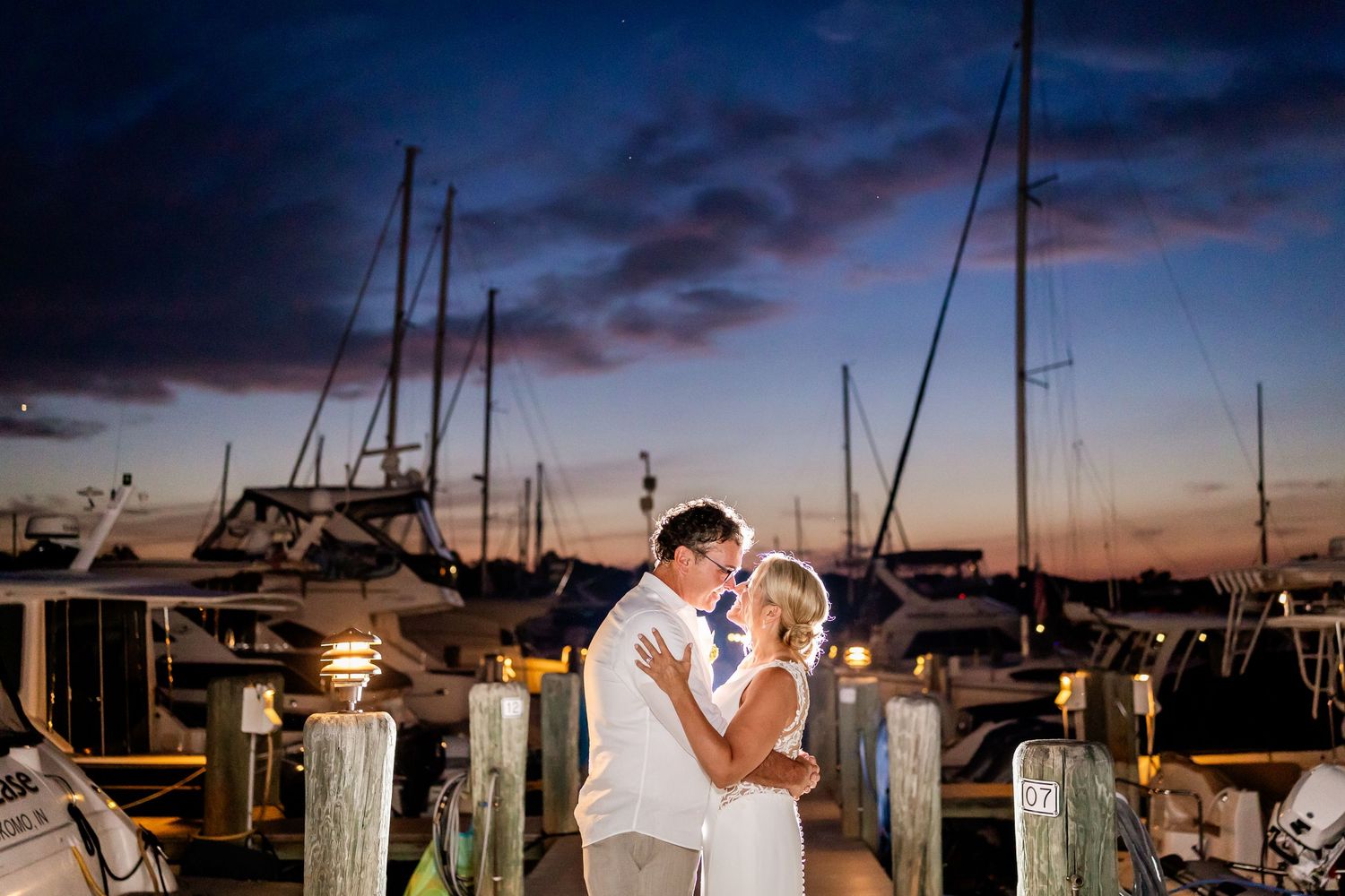 A romantic sunset wedding celebration at a marina with boats and glowing string lights creating an elegant atmosphere.