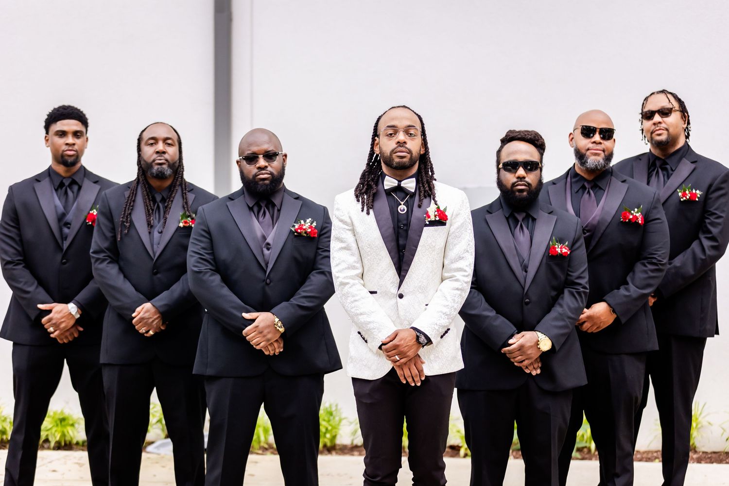 Groomsmen in dark suits with red accents pose with one in white jacket.