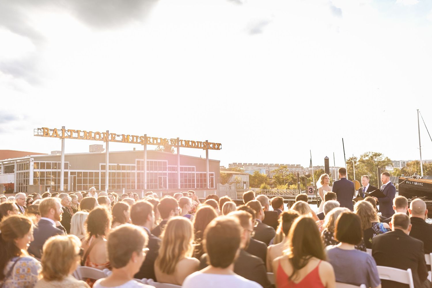 Large crowd at an outdoor music festival venue during sunset with warm golden lighting.