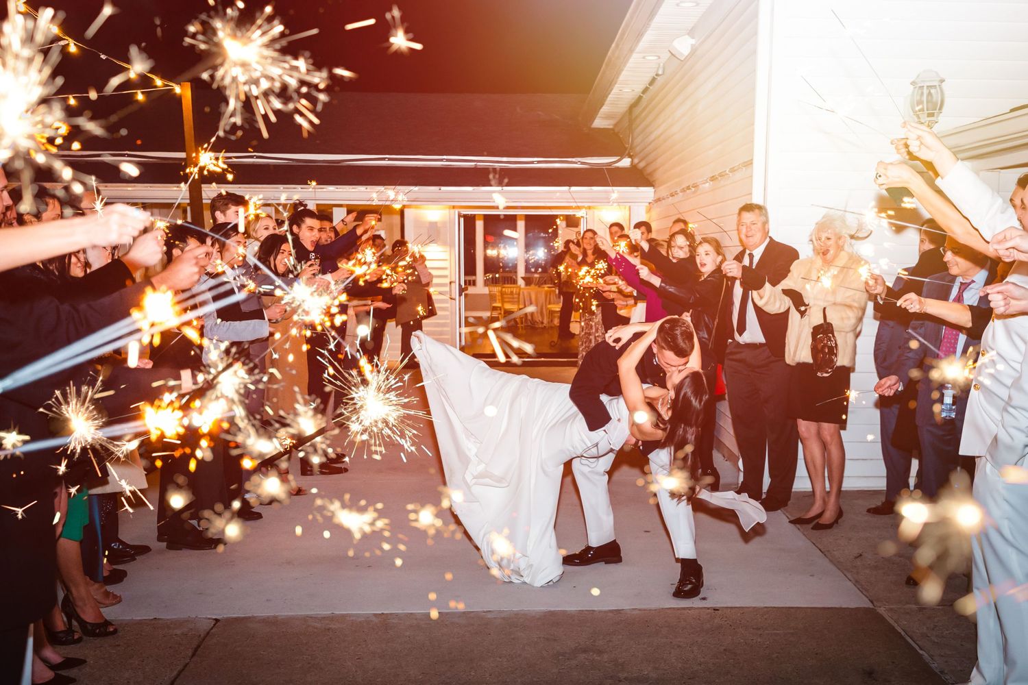Wedding guests hold sparklers creating a magical tunnel as a couple walks through during their evening reception celebration.