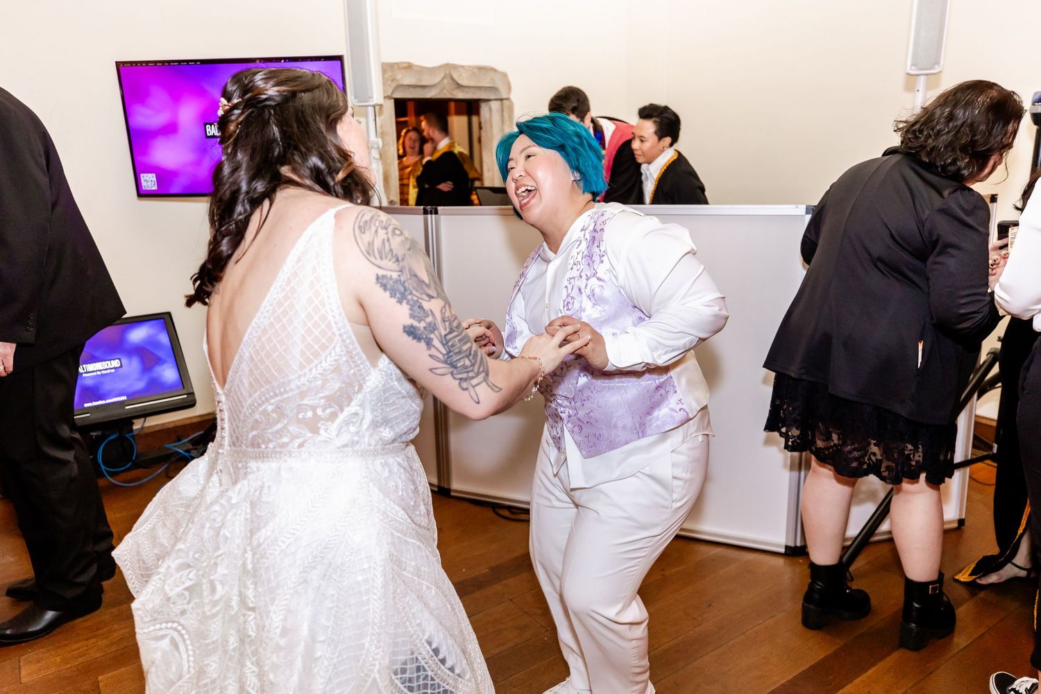Guests in white and formal attire dance together during an indoor celebration.