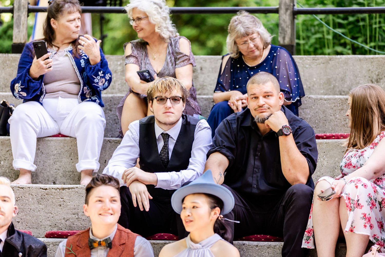 Group of wedding guests sitting casually on outdoor concrete steps.