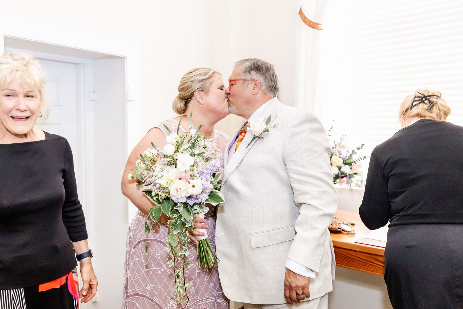 Intimate moment during a wedding ceremony in a bright indoor venue with floral decorations.