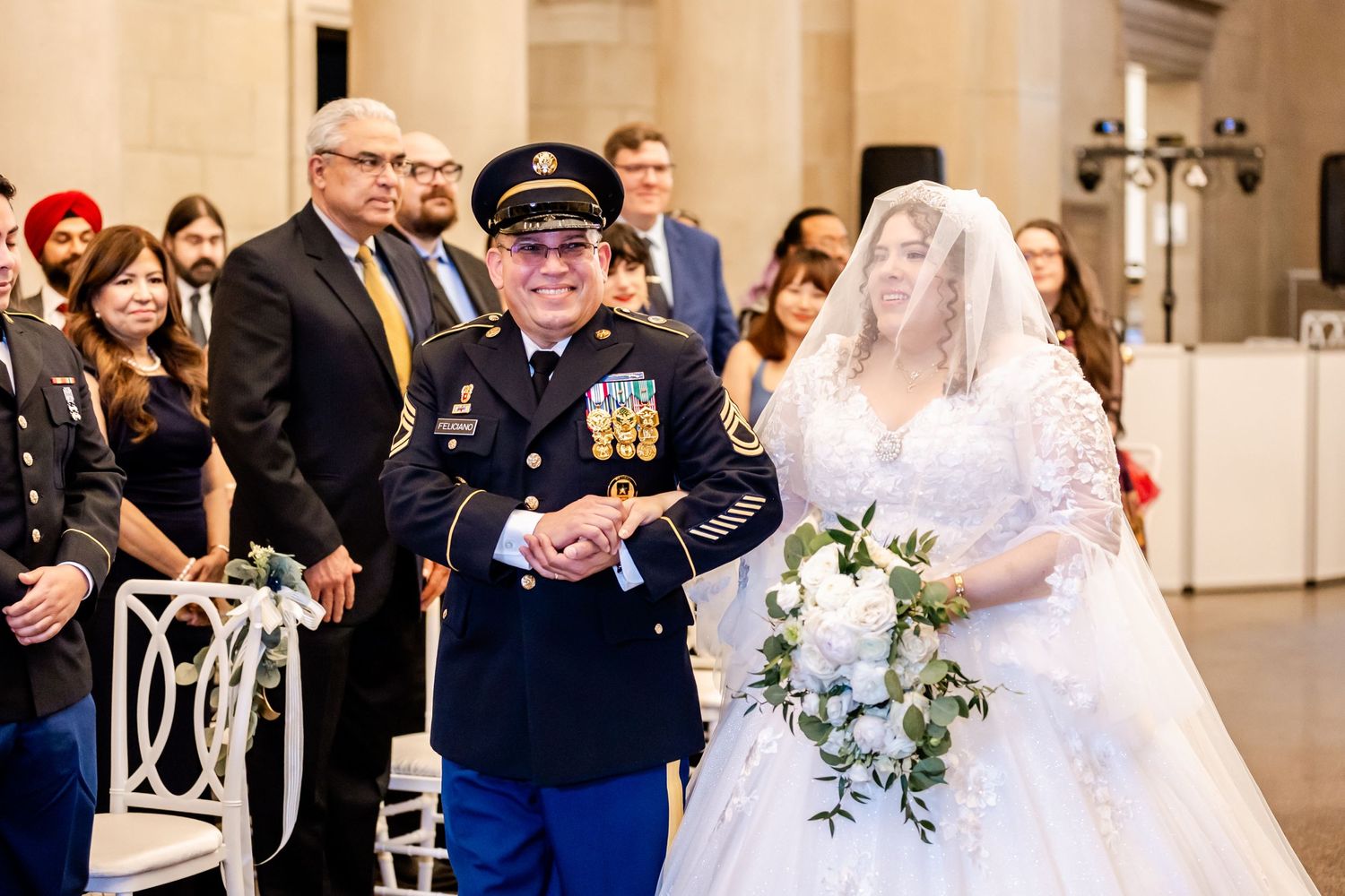 Military officer and bride in traditional white gown exchange vows during indoor ceremony.