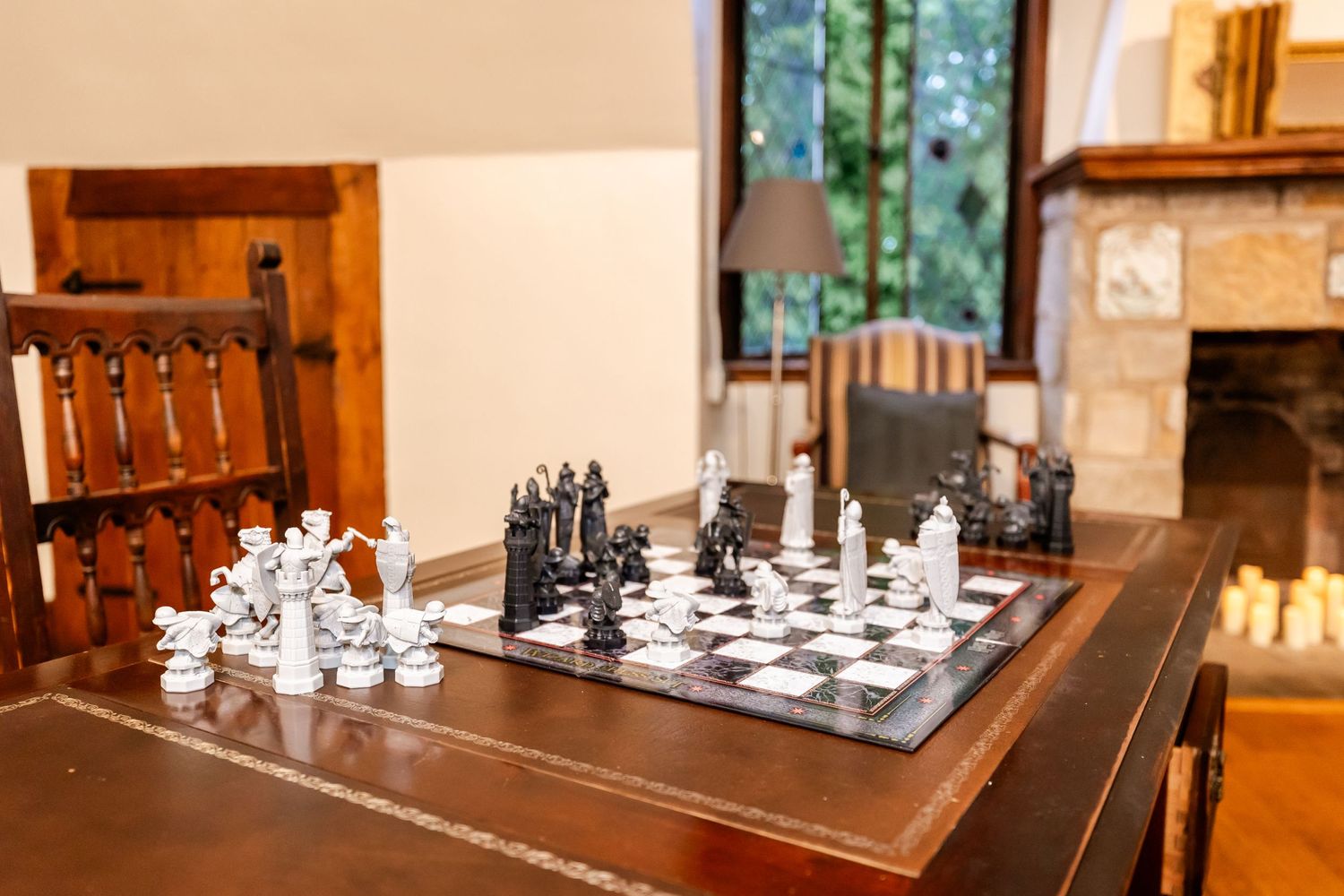 Black and white chess pieces set up on a wooden chess board in an elegant room.