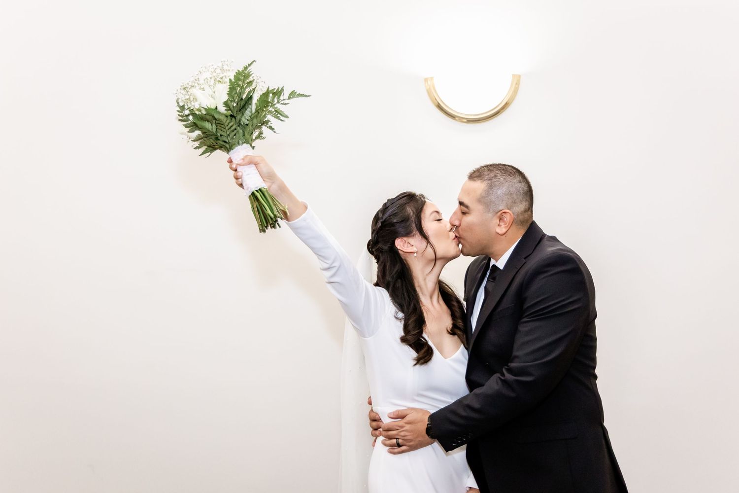 Couple shares romantic moment as bride raises bouquet during wedding photo session.