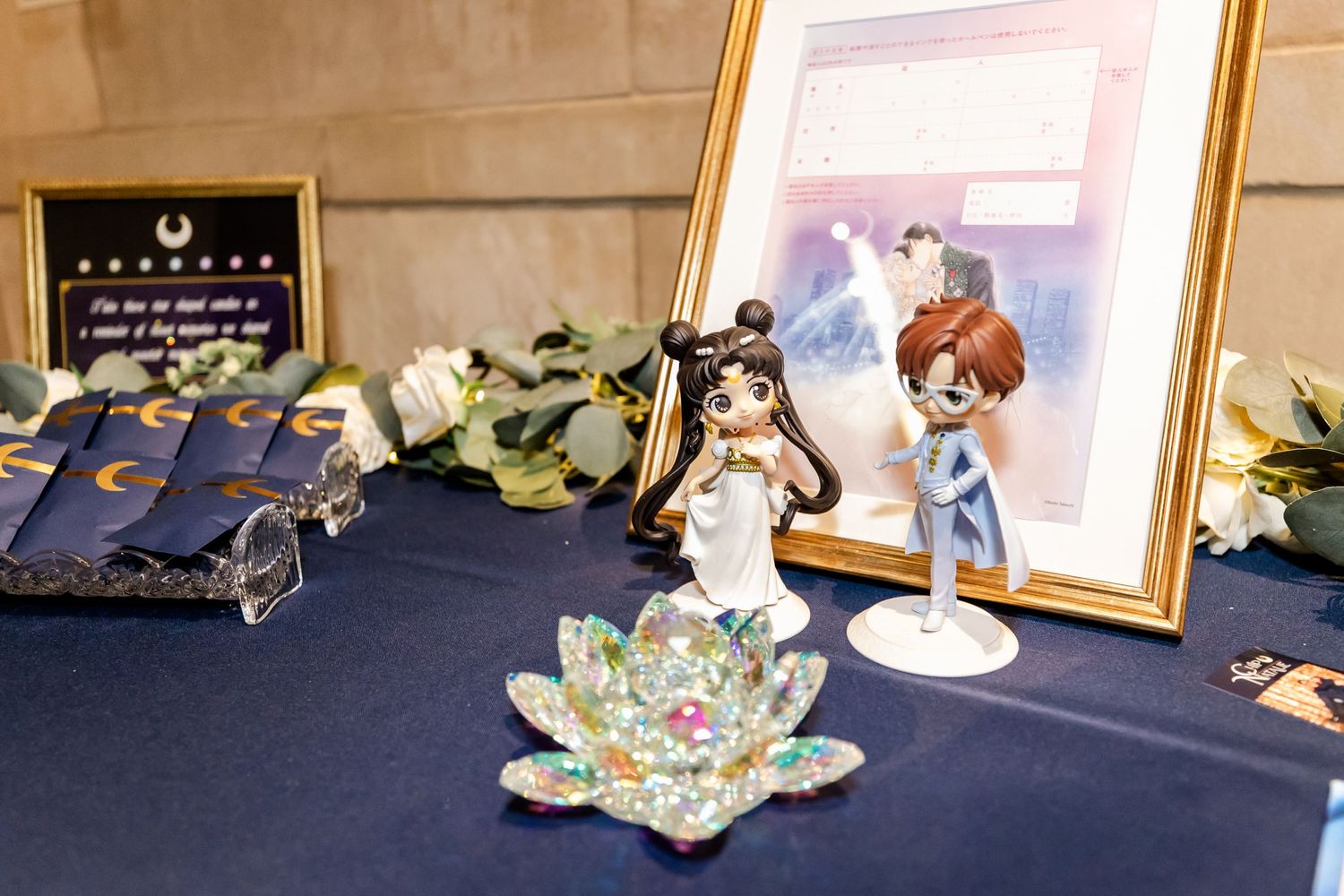Decorative display items including a crystal lotus flower and framed artwork on a navy blue tablecloth.