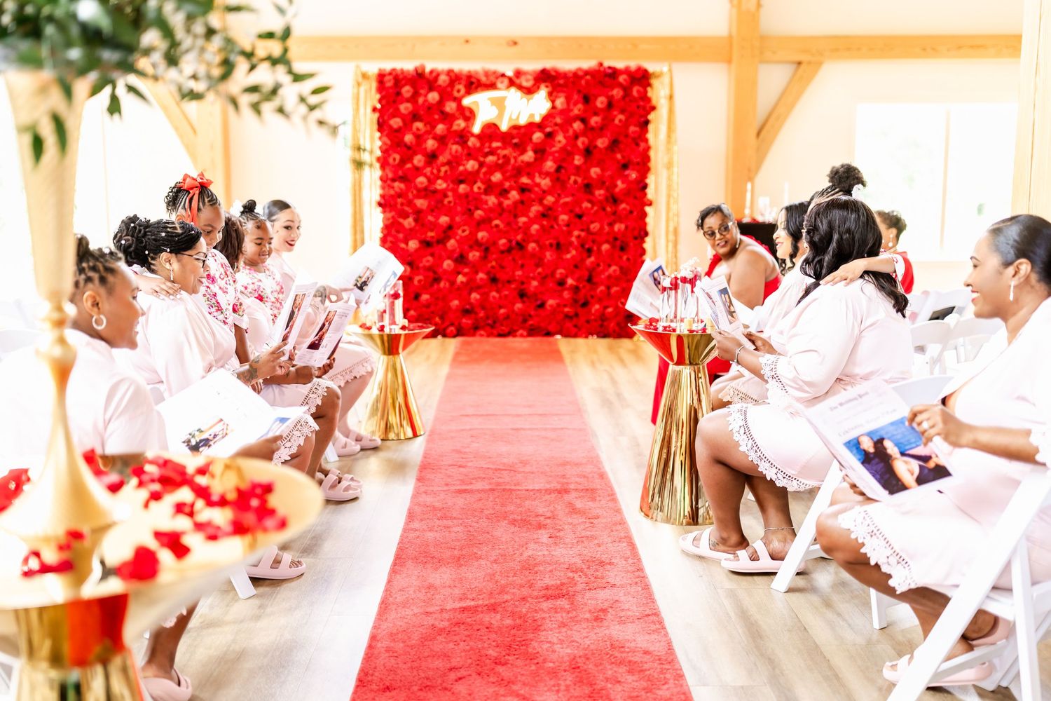 Wedding ceremony setup with red carpet aisle and heart-shaped backdrop as guests sit in white chairs.