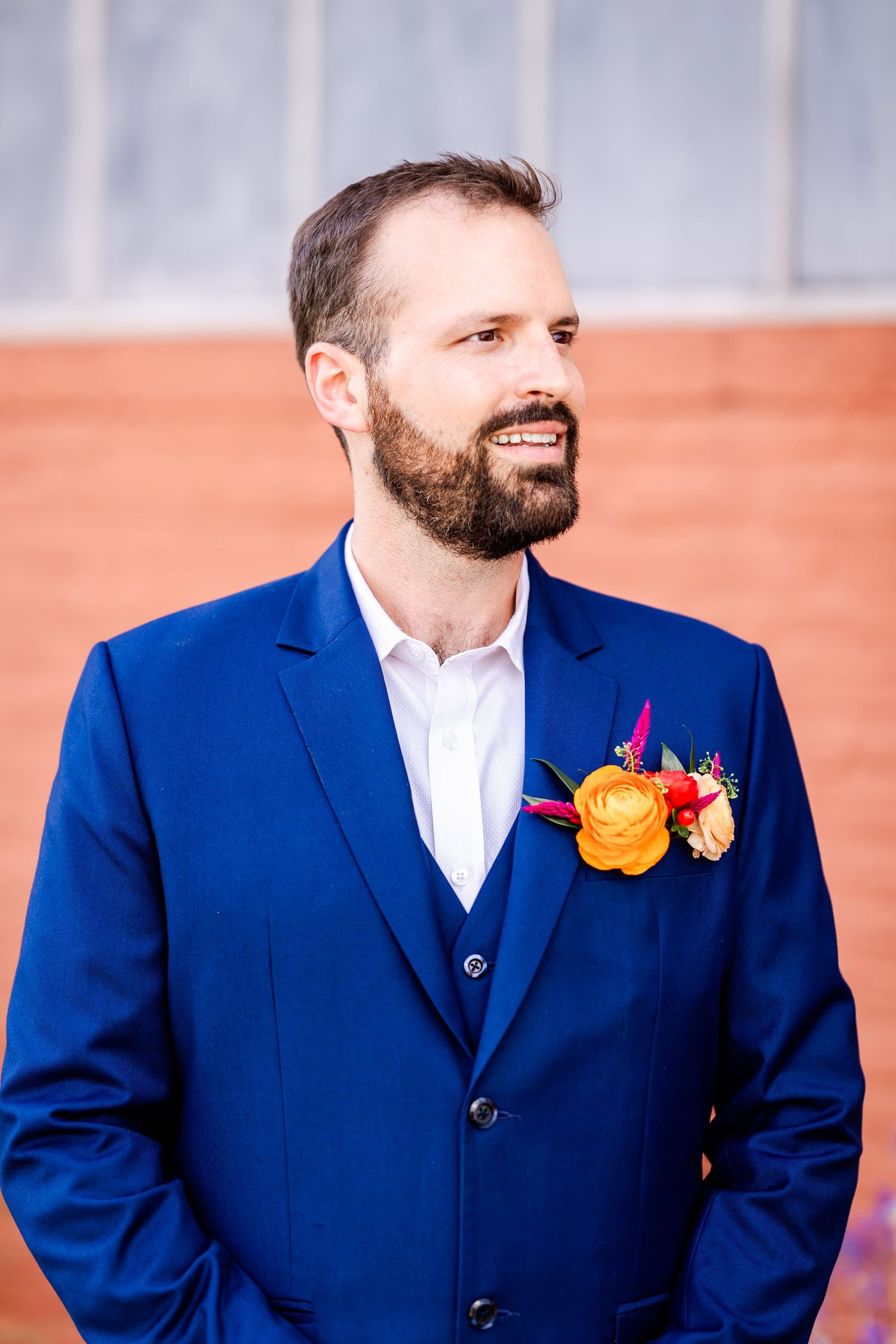 Groom in navy blue suit wearing vibrant yellow and pink floral boutonniere.