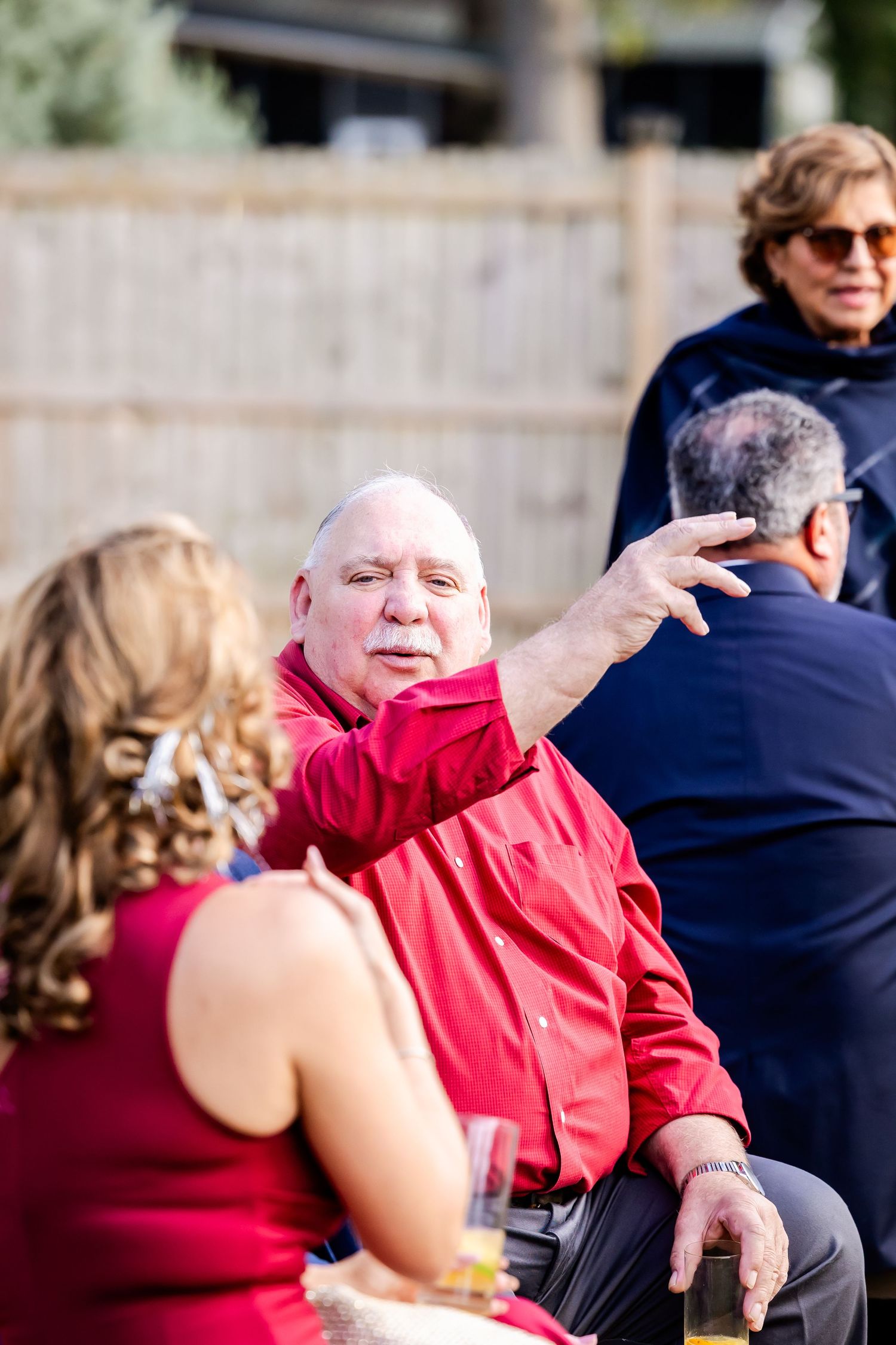 A guest in a red jacket gestures while conversing at an outdoor event.