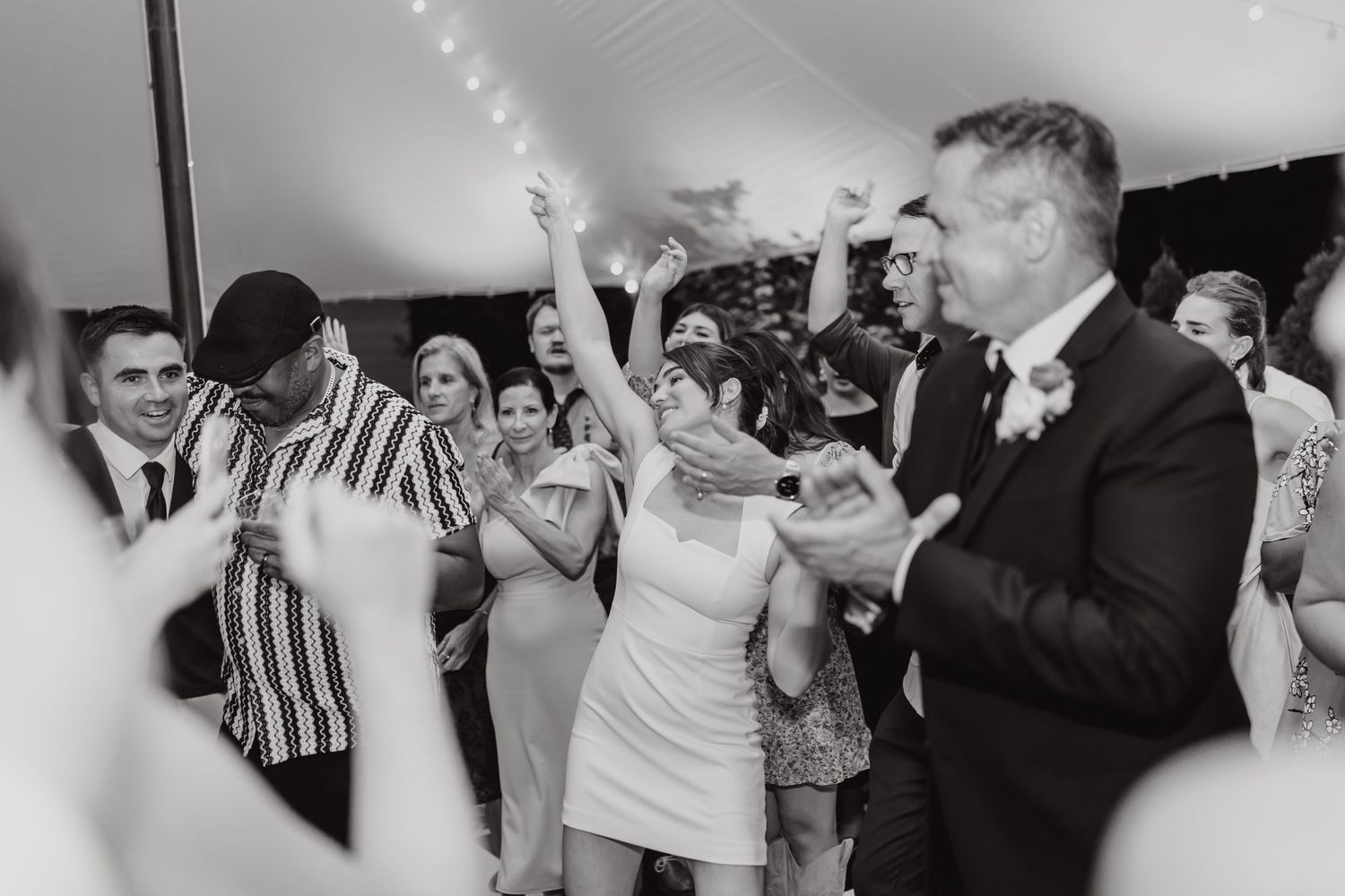 Black and white photo of wedding guests dancing and celebrating on reception dance floor.