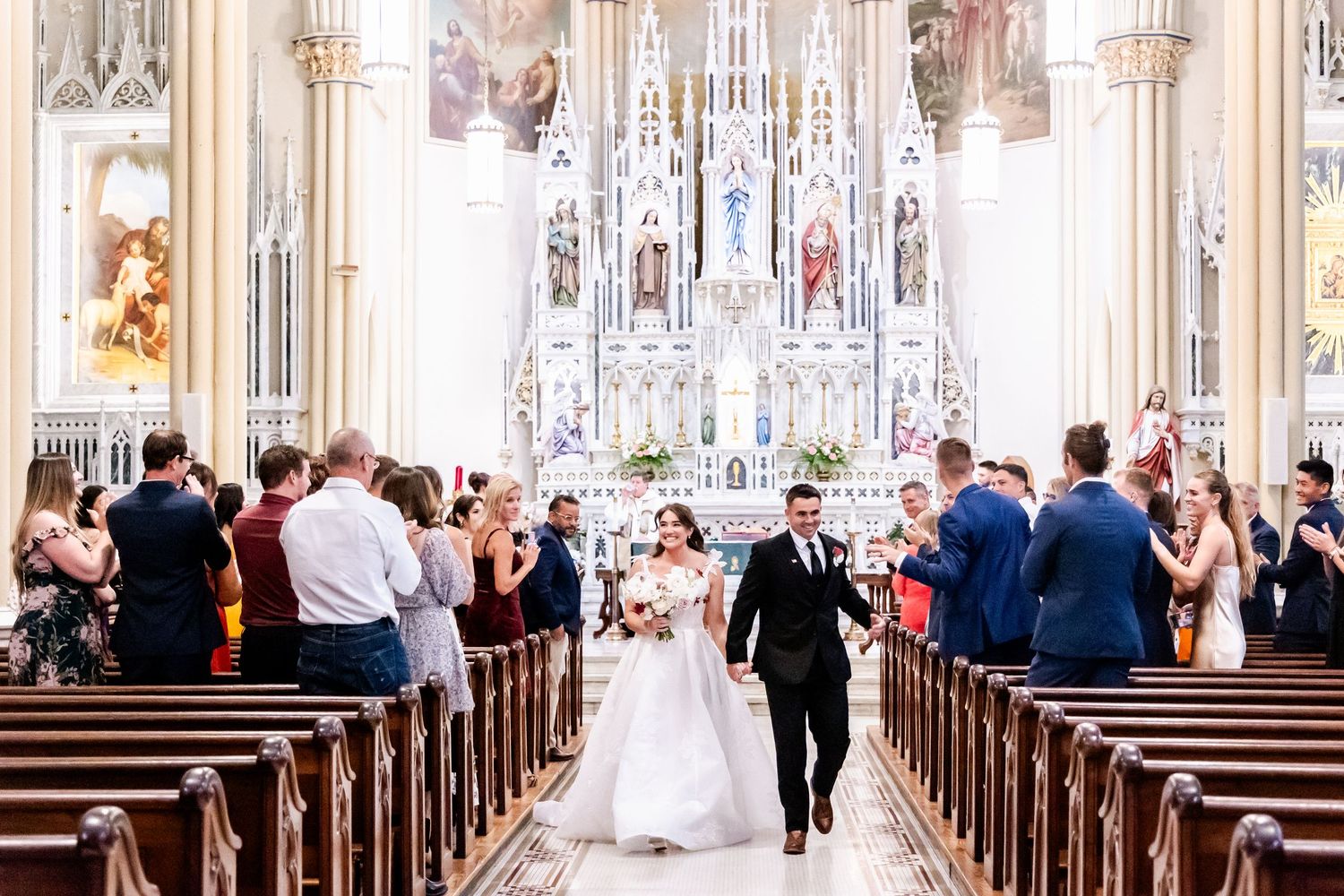 Wedding guests seated in wooden pews inside a majestic cathedral with soaring arched ceilings.