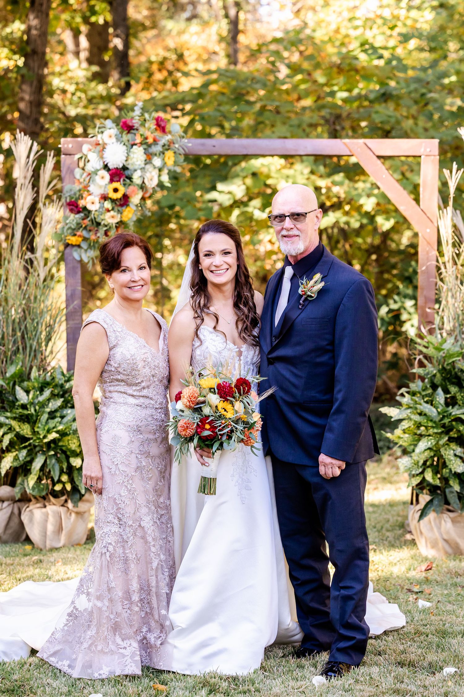 Wedding party poses under wooden arch with autumn foliage in background.