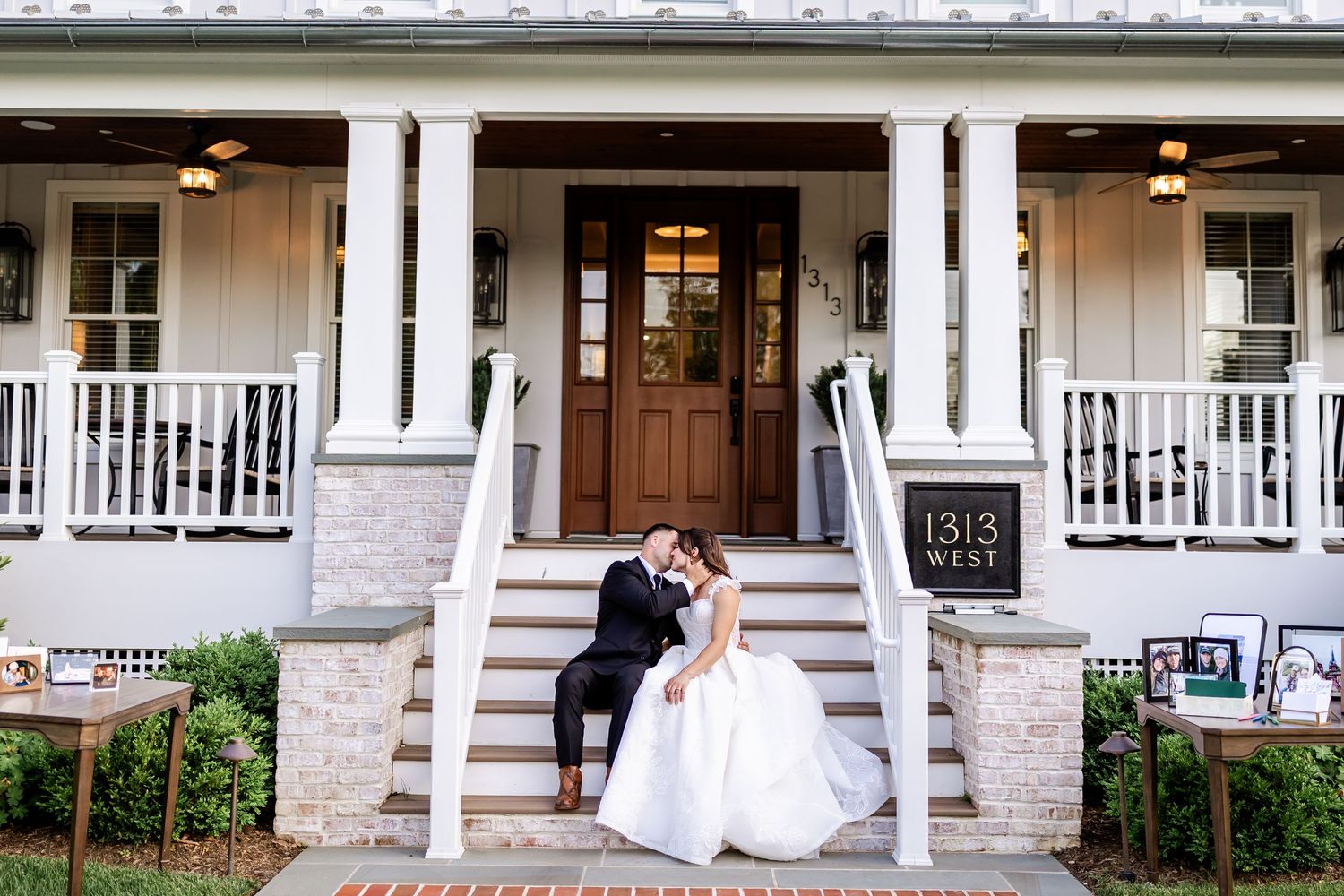 Classic white house with stone foundation and wraparound porch serves as wedding venue backdrop.