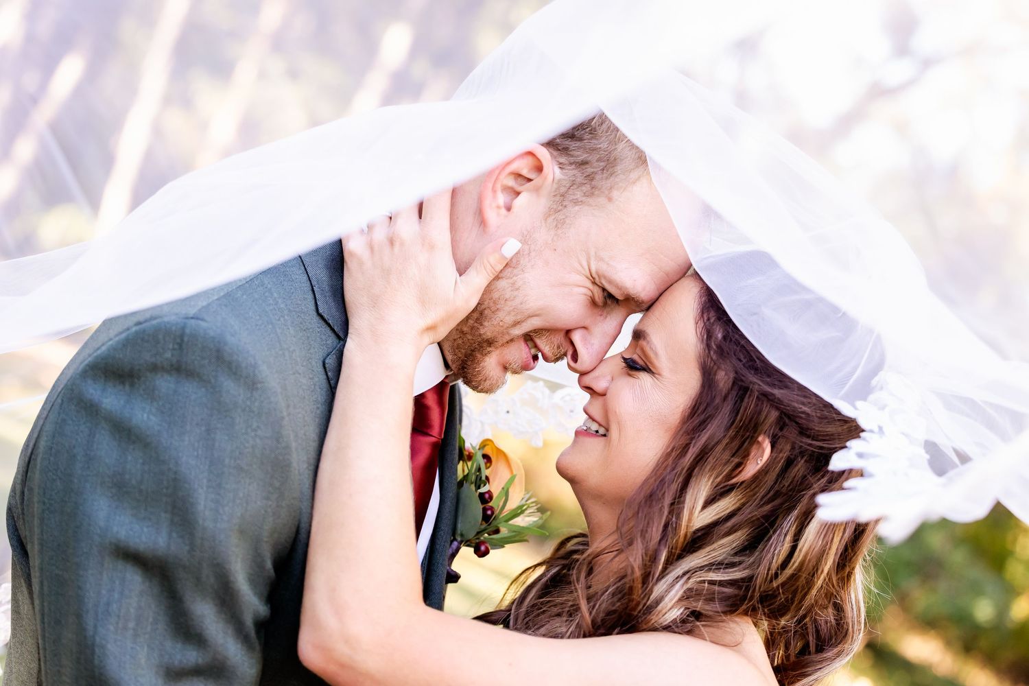 An intimate wedding portrait showing a couple's romantic moment beneath a flowing white veil.