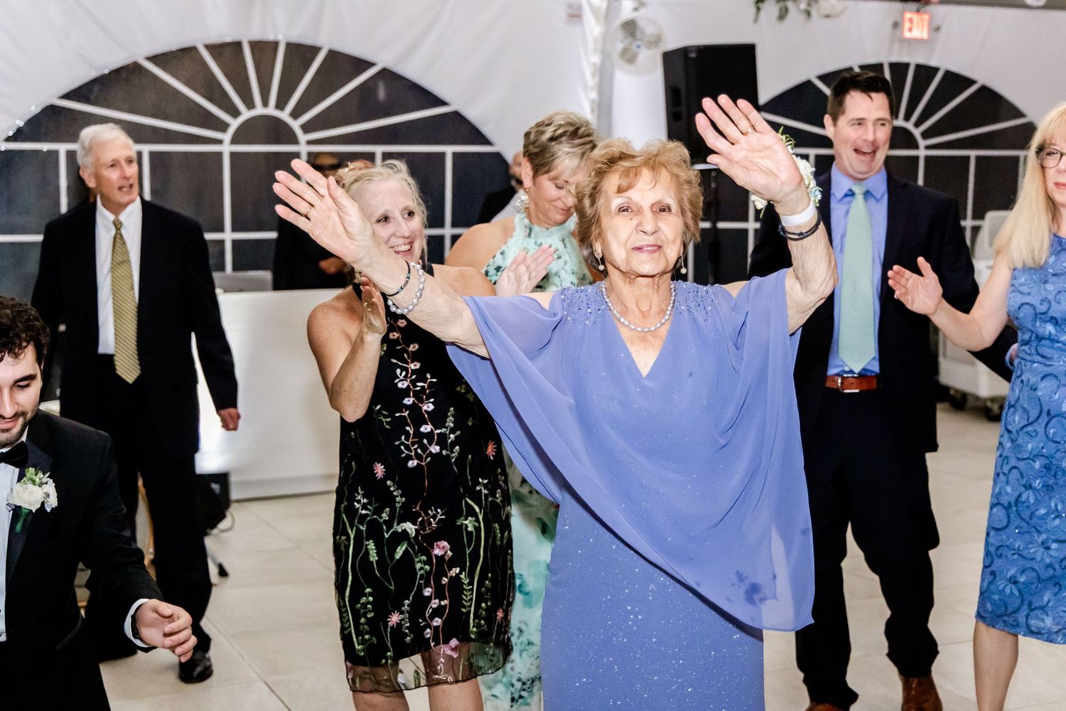 Wedding reception guests dancing and celebrating on the dance floor under white tent.