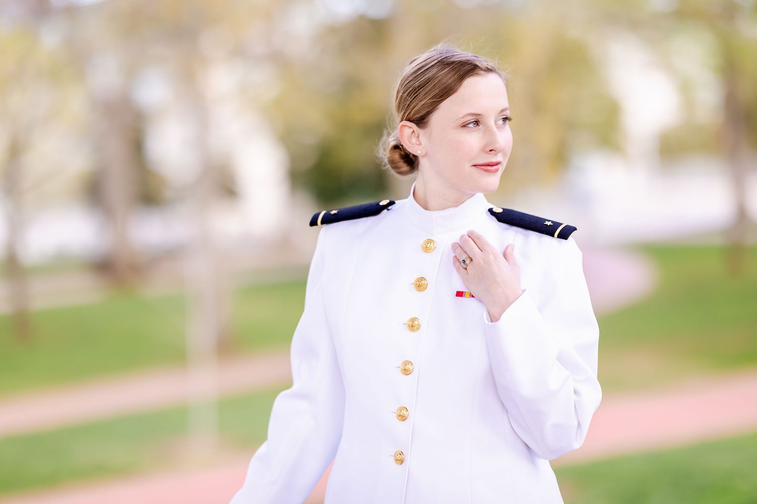 Naval officer in crisp white dress uniform poses outdoors with a warm smile in natural lighting.