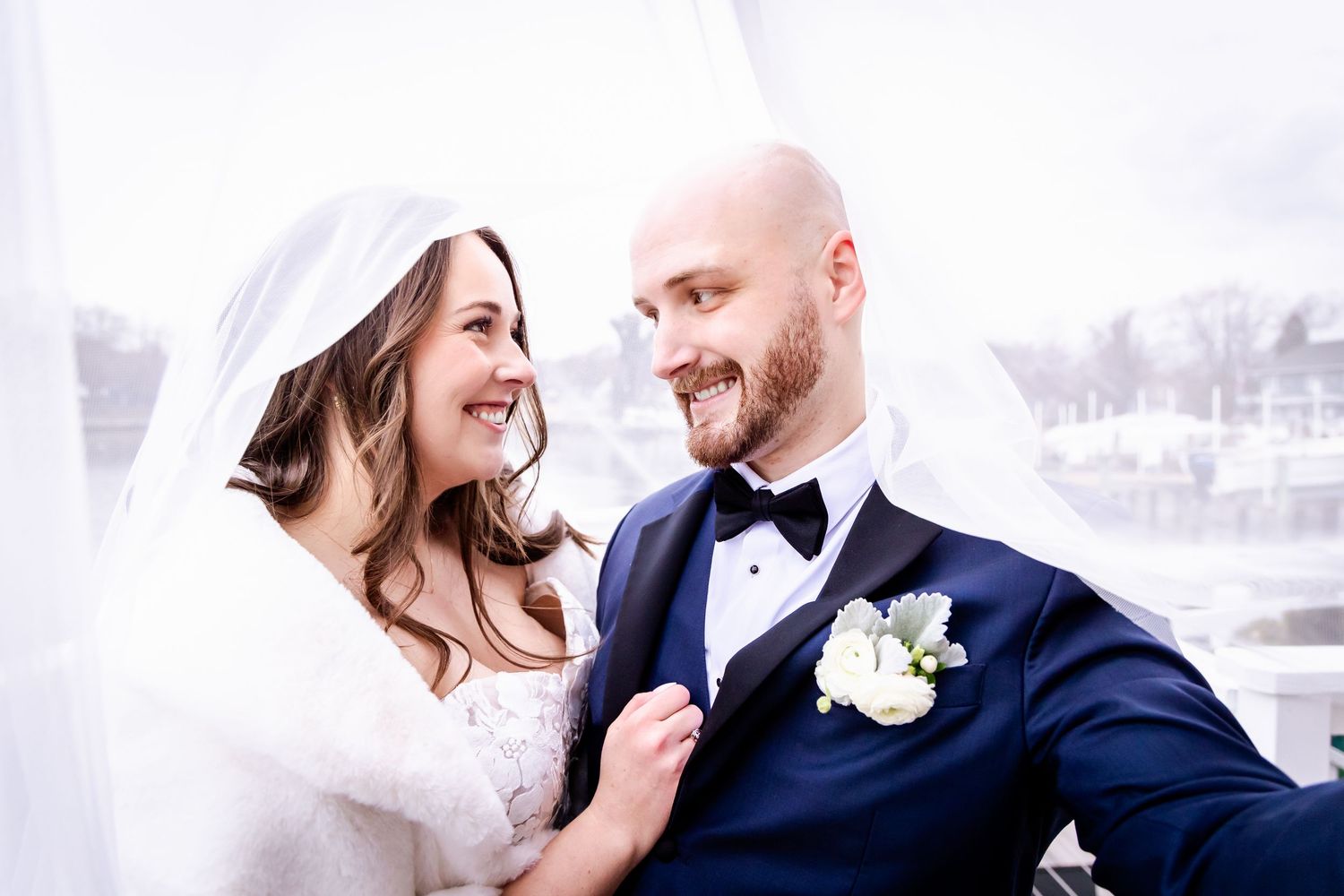 A happy couple shares a joyful moment together on their wedding day wearing formal attire with a white veil flowing.