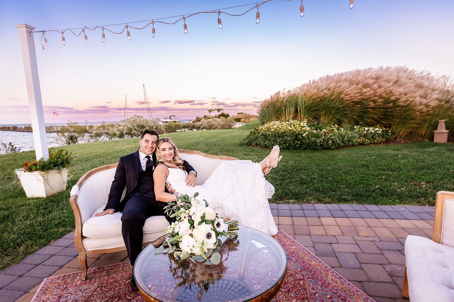 A couple in wedding attire shares romantic moments on a wooden pier at sunset by the ocean.