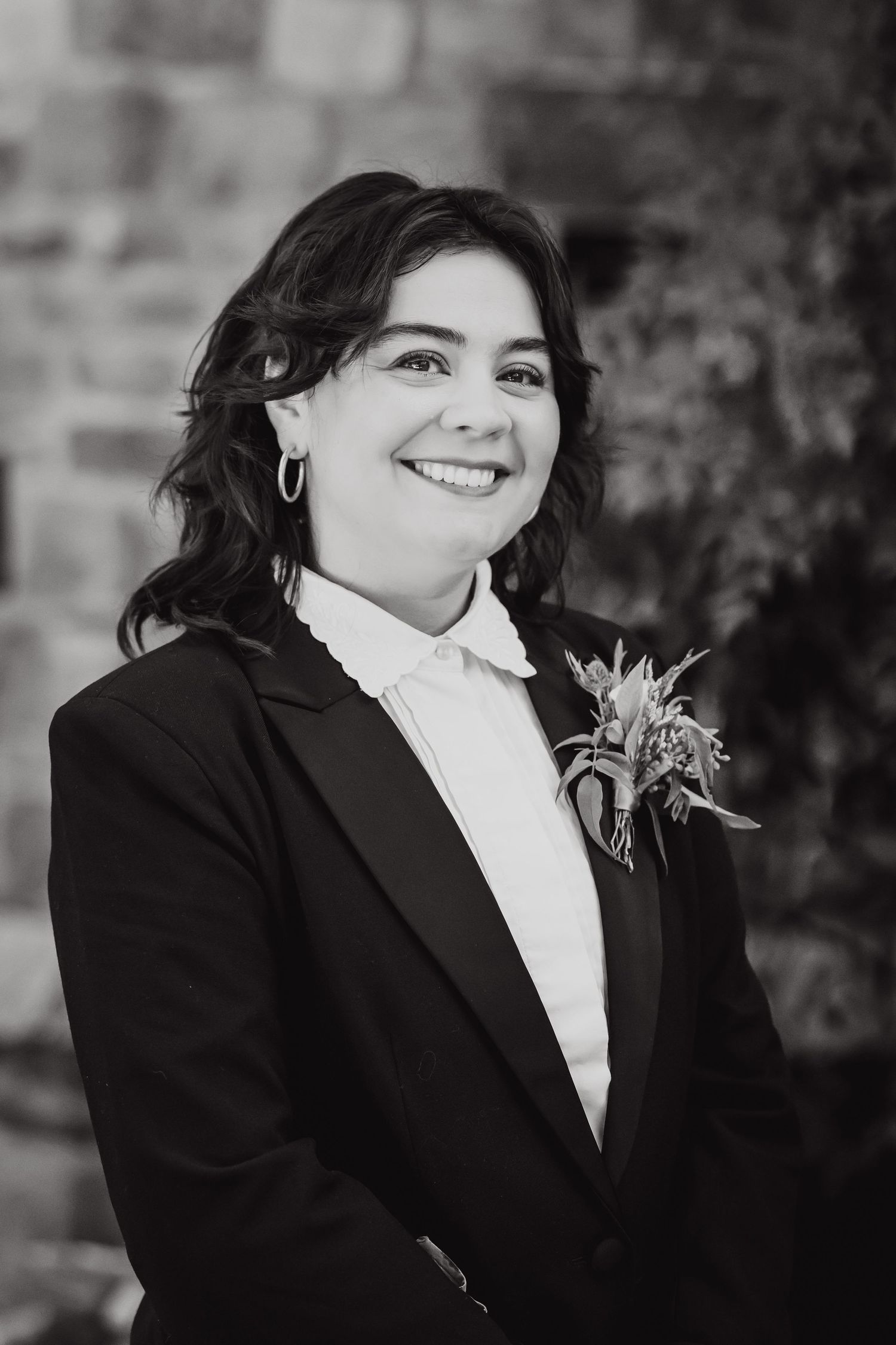 Professional portrait in black and white showing formal attire with a boutonniere against a brick wall background.