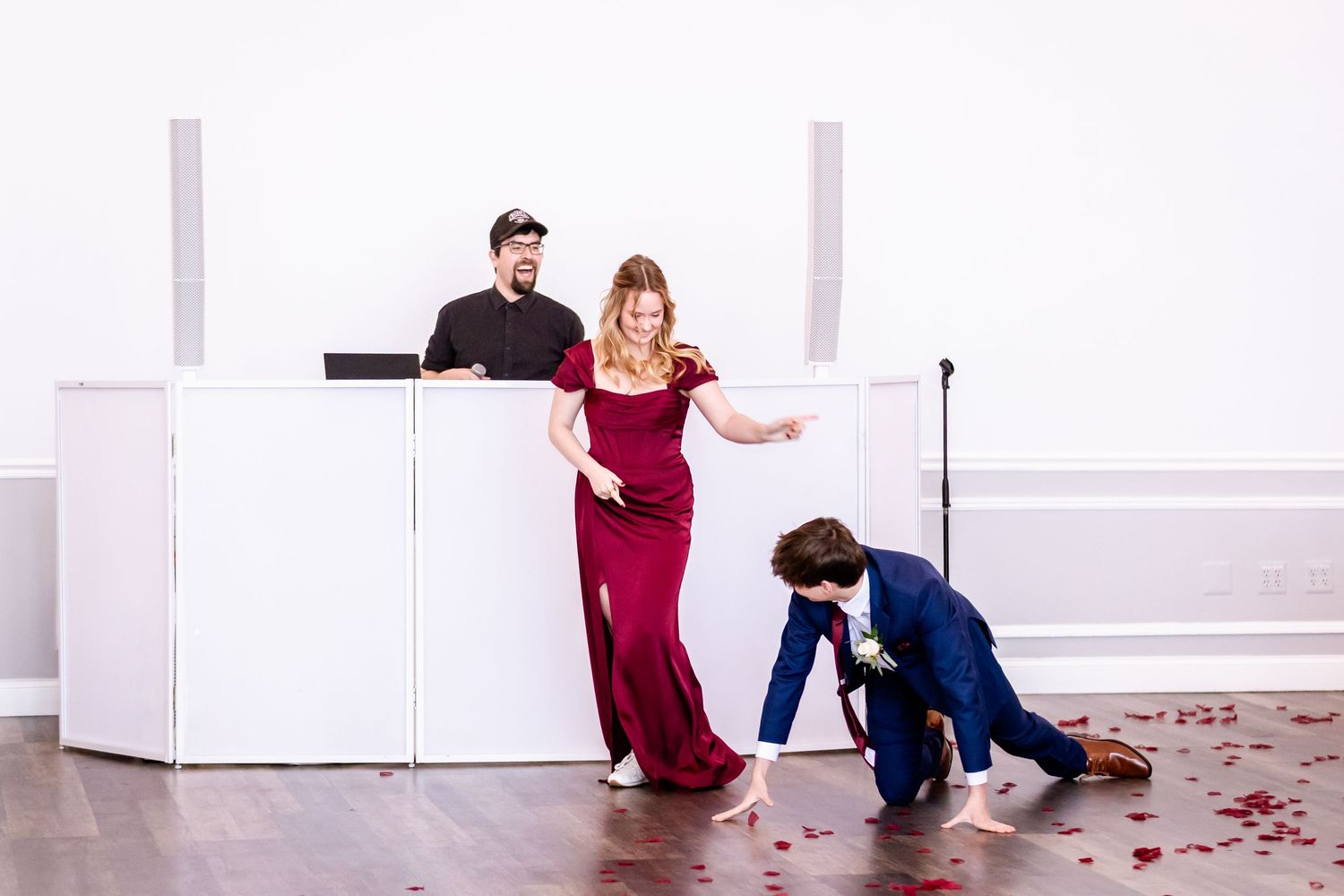 Wedding party members in burgundy and navy performing fun poses in a white modern venue.