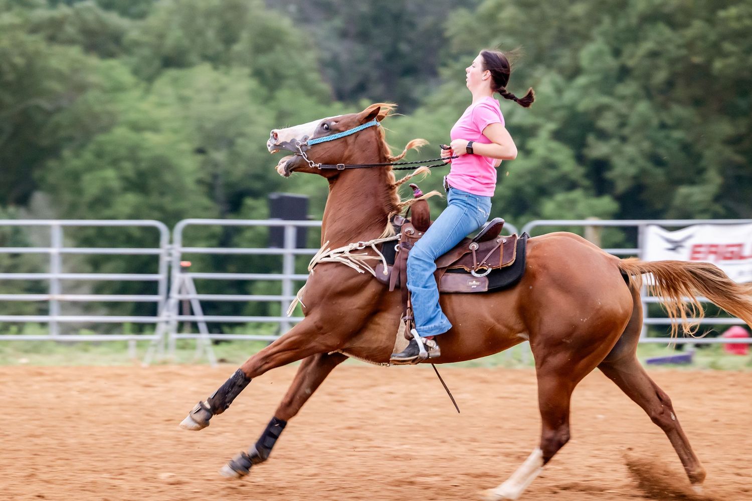 Rider on chestnut horse galloping at speed through sandy arena.