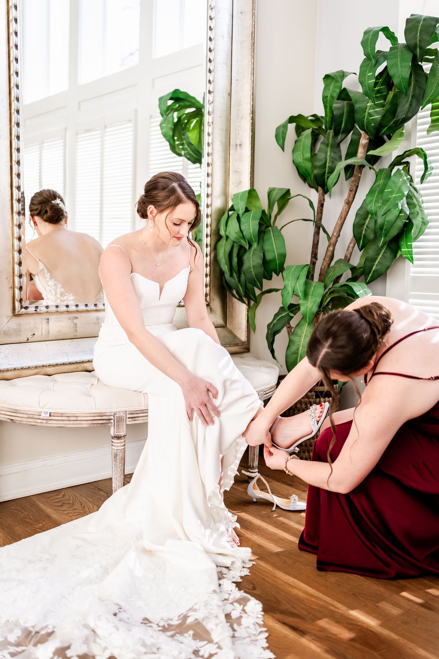 Wedding preparation scene showing dress adjustments in a bright interior room with indoor plants.