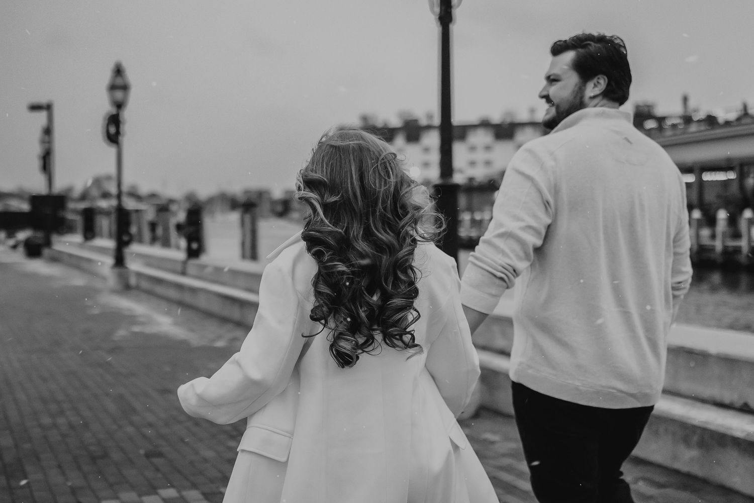 Black and white photos show a romantic couple walking and embracing along a waterfront boardwalk.