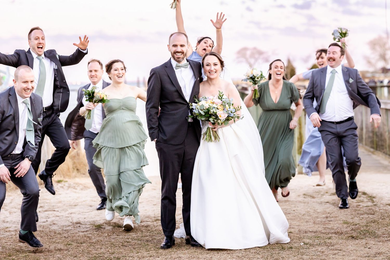 Energetic wedding party running and celebrating together outdoors in coordinated formal attire.