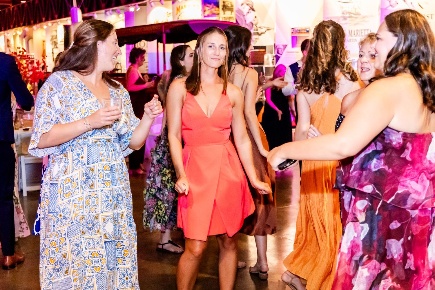 People in colorful dresses dancing at a festive indoor celebration with pink lighting and decorative elements.