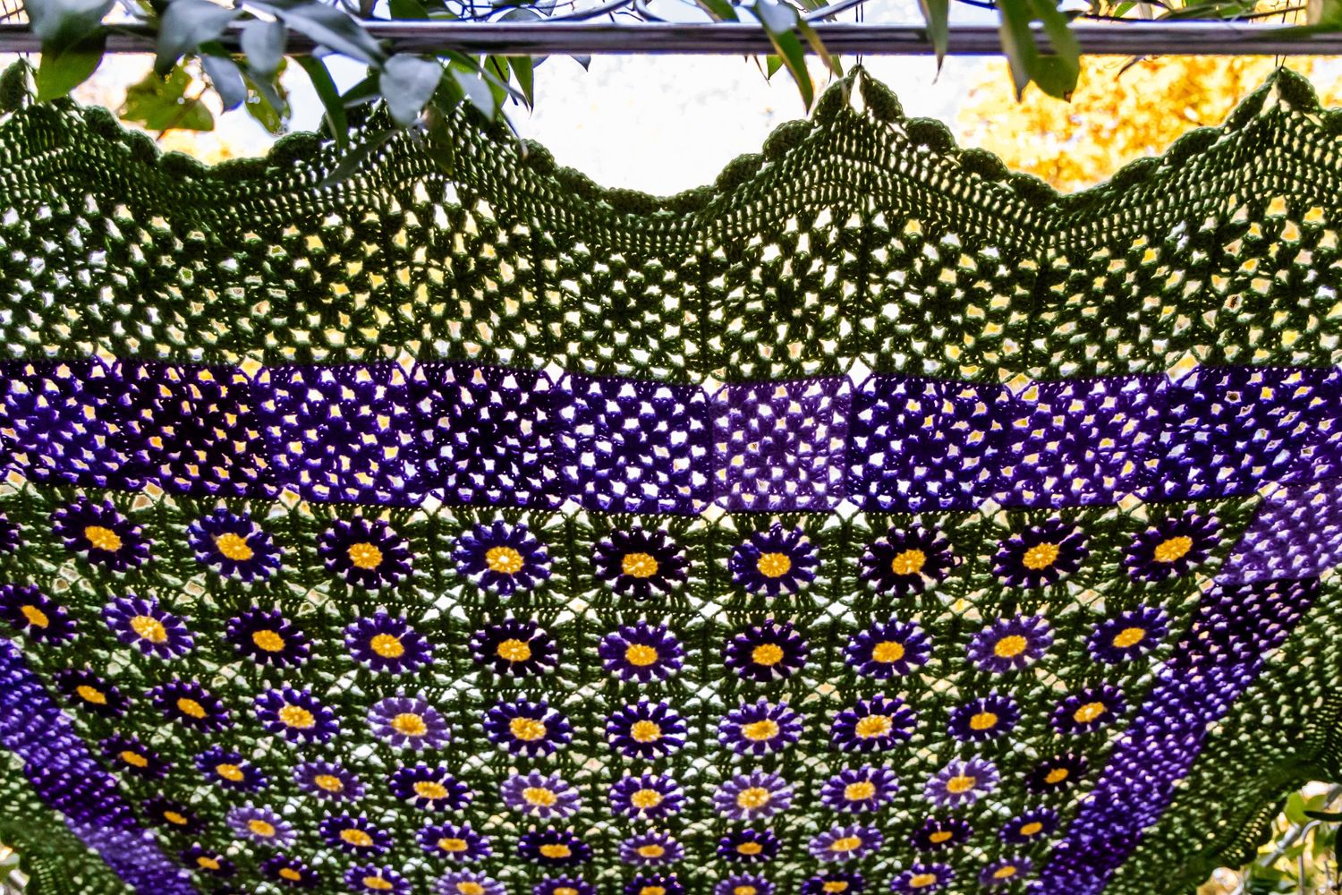 Detailed view of a colorful knitted or crocheted textile with purple, green and floral patterns.