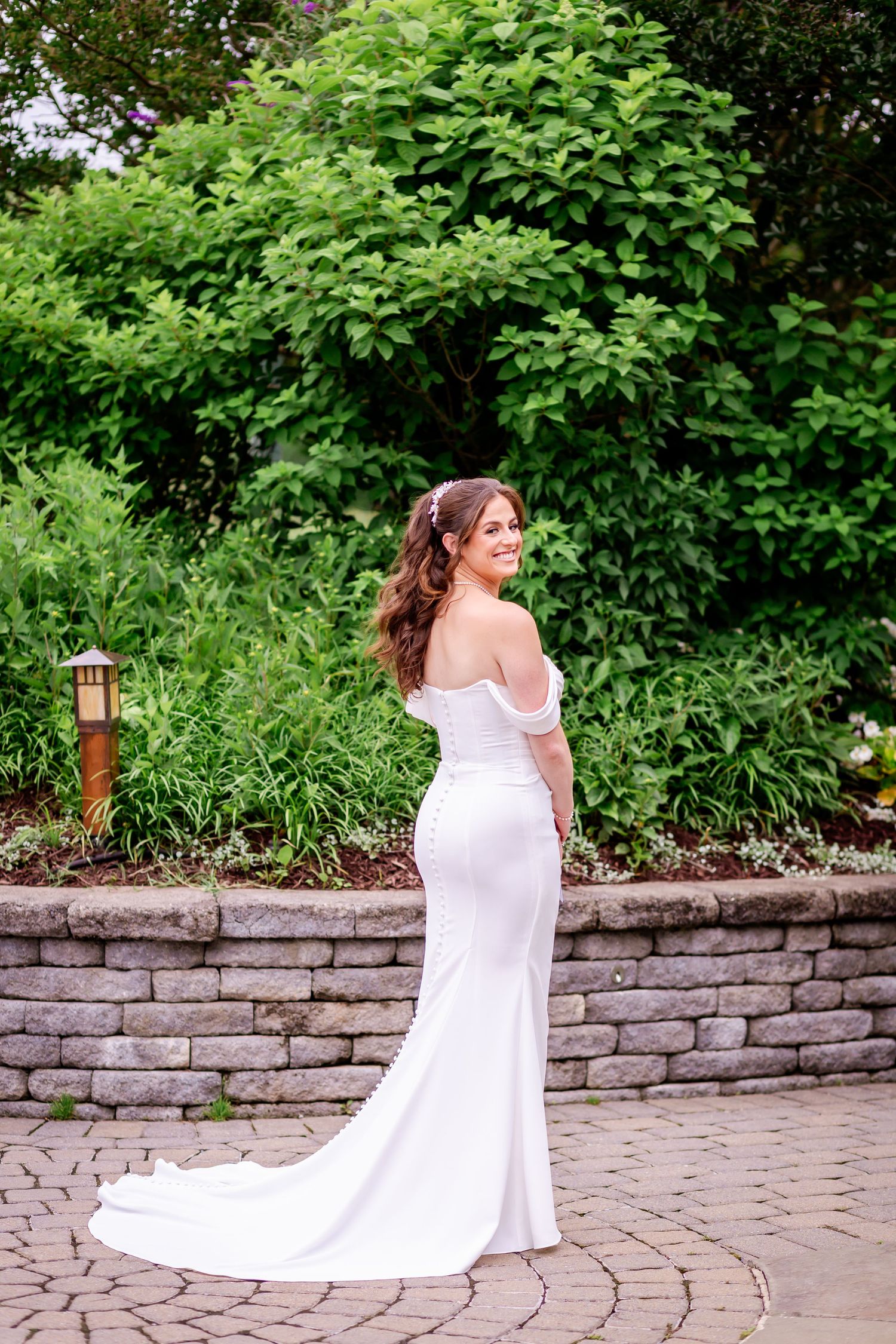 A flowing white wedding dress with train is captured in a sequence of photos against a stone wall and greenery.