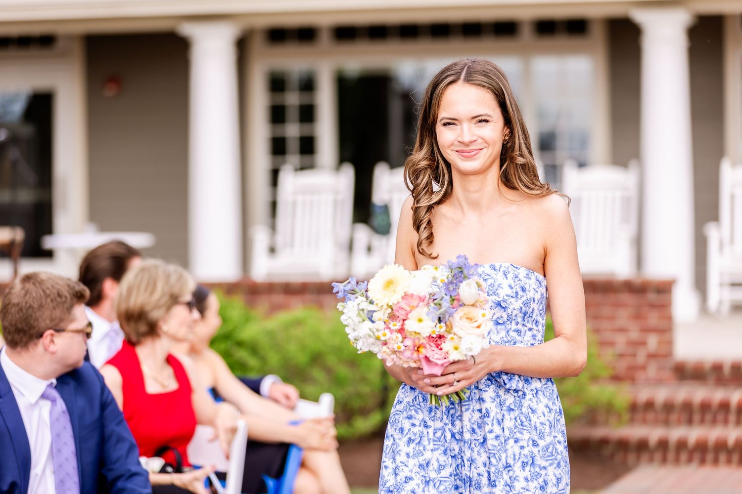 Wedding guests mingling on a porch with white columns during an outdoor reception.