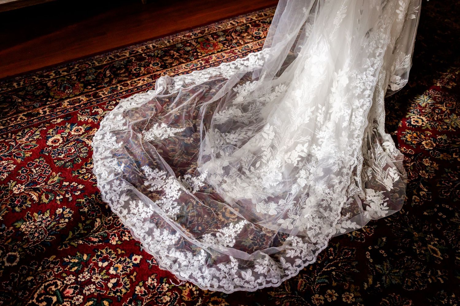 Delicate white lace wedding dress train with intricate floral patterns spread across a traditional Persian rug.