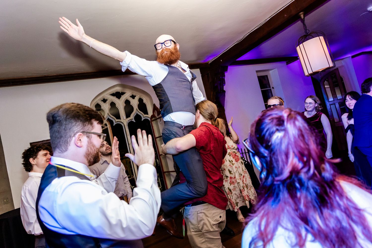 People dancing and celebrating at a wedding reception with purple lighting and energetic party atmosphere.