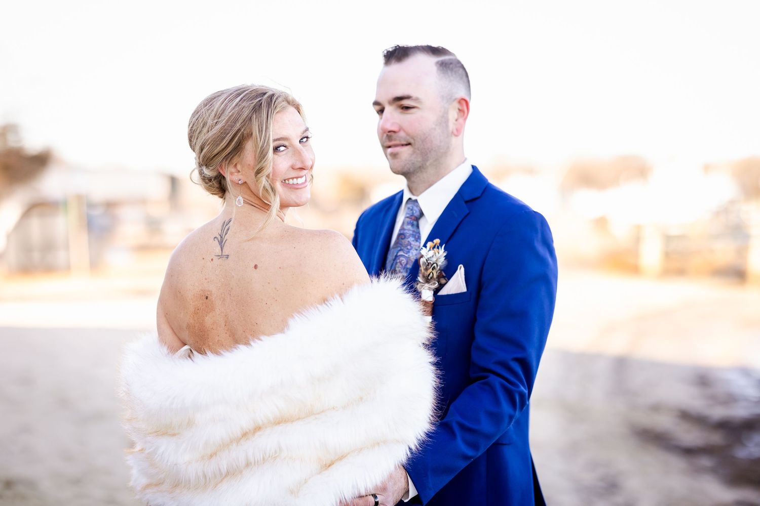 A couple in formal wedding attire embrace during a sunset photoshoot in a snowy winter landscape.